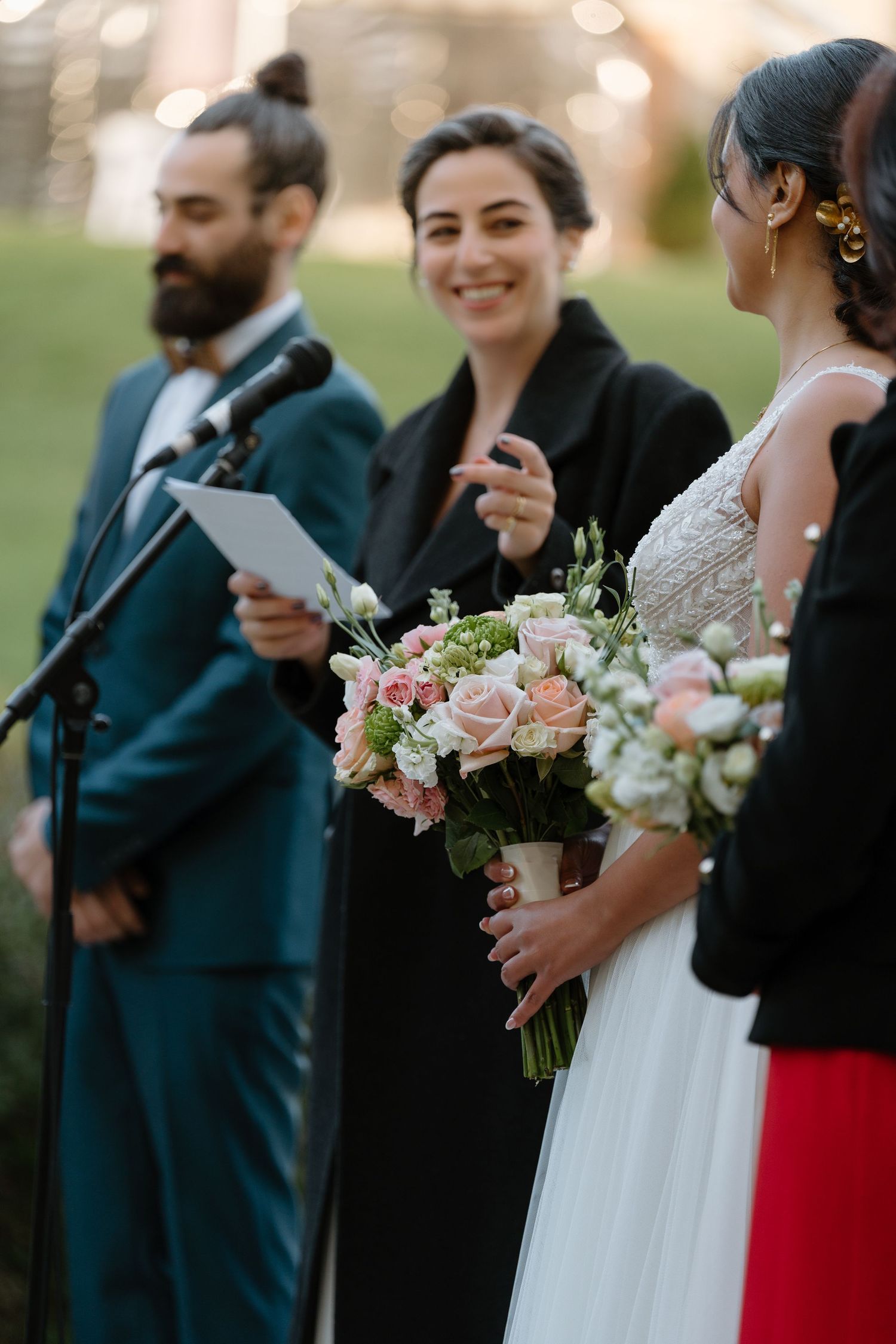 Wedding party members standing at microphone during outdoor ceremony.