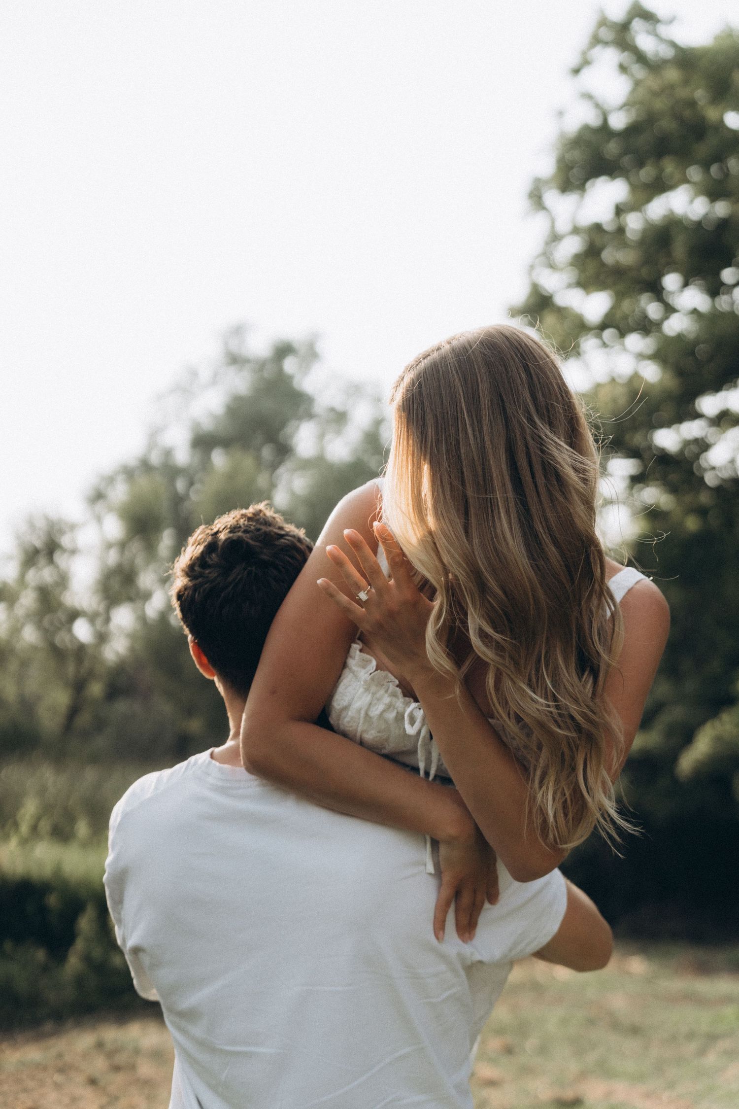 A couple in white clothing embraces outdoors in soft natural lighting during a romantic photoshoot.