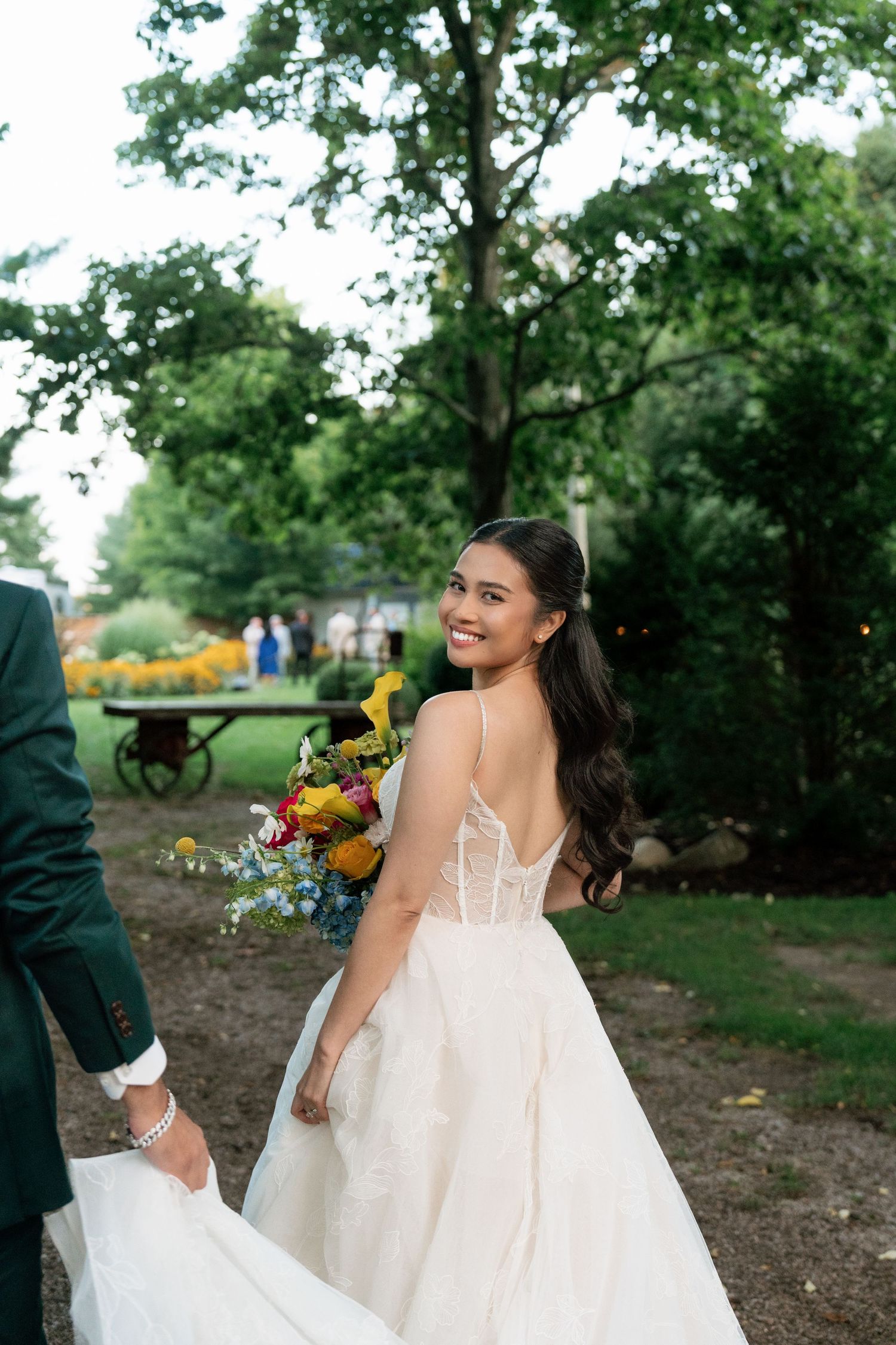A joyful bride in a white lace gown twirls playfully in an outdoor garden setting.