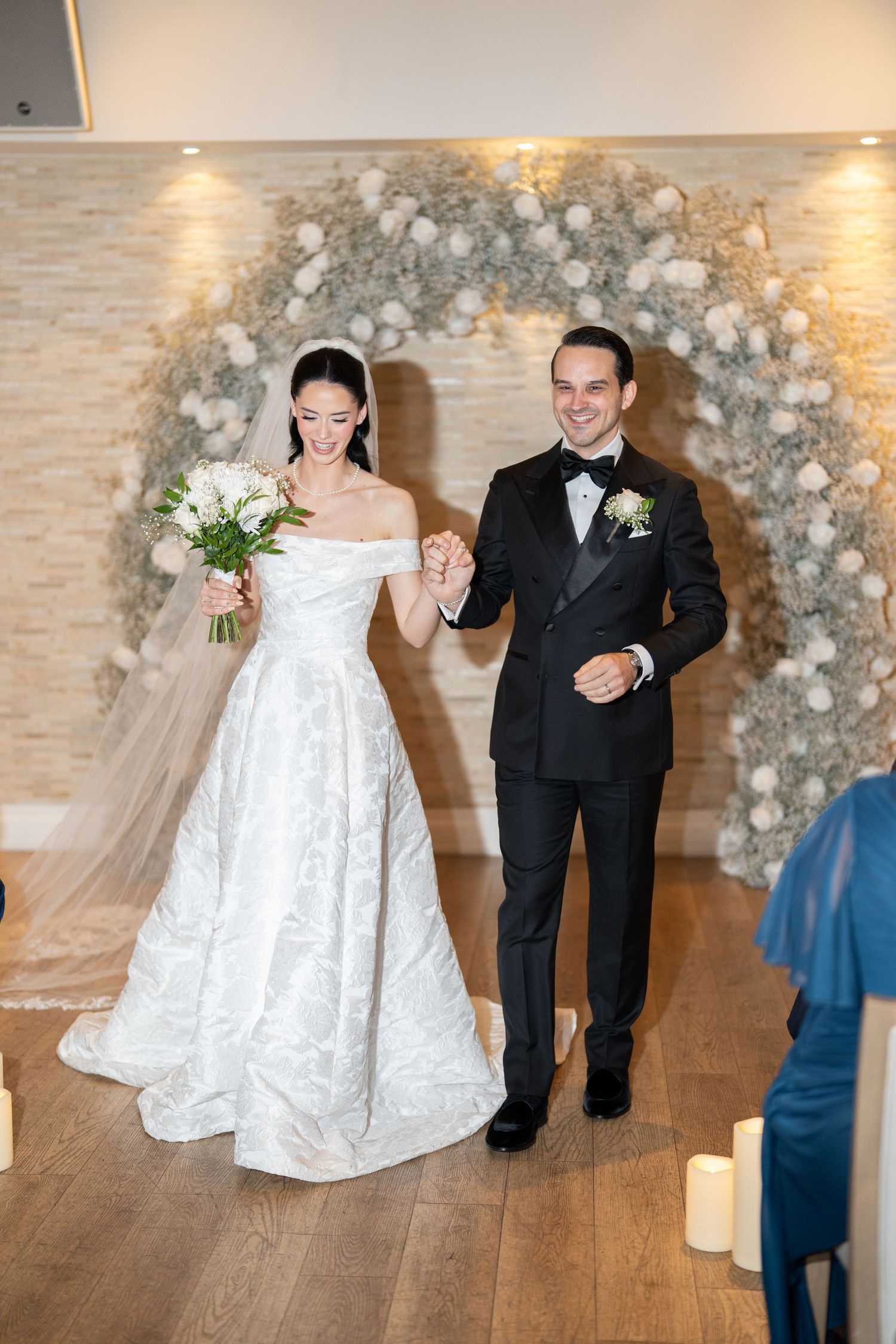 A couple dances together on a wooden floor under a decorative balloon arch during their wedding celebration.