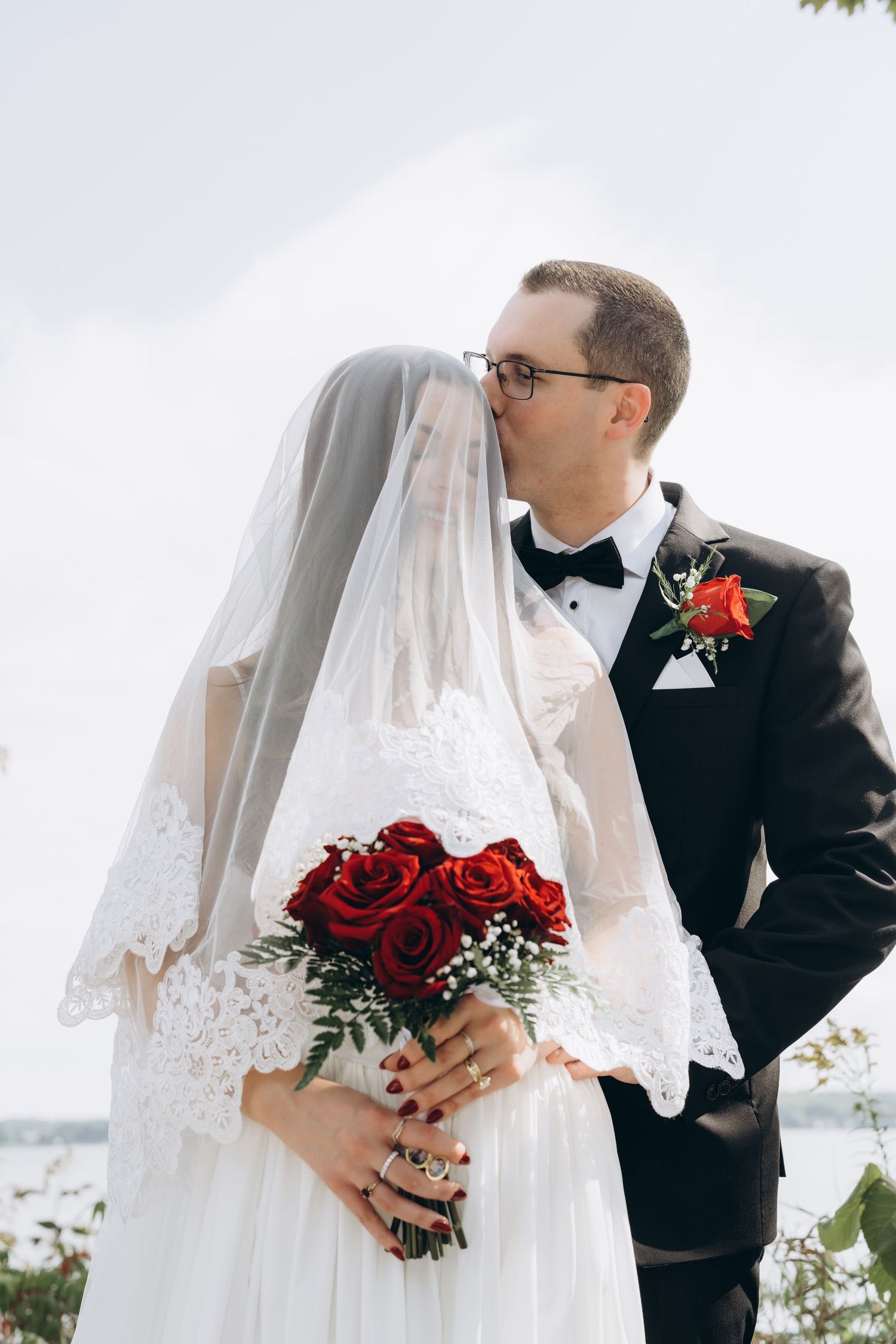 A romantic wedding photo series showing tender moments between a newly married couple with red roses and a lace veil.