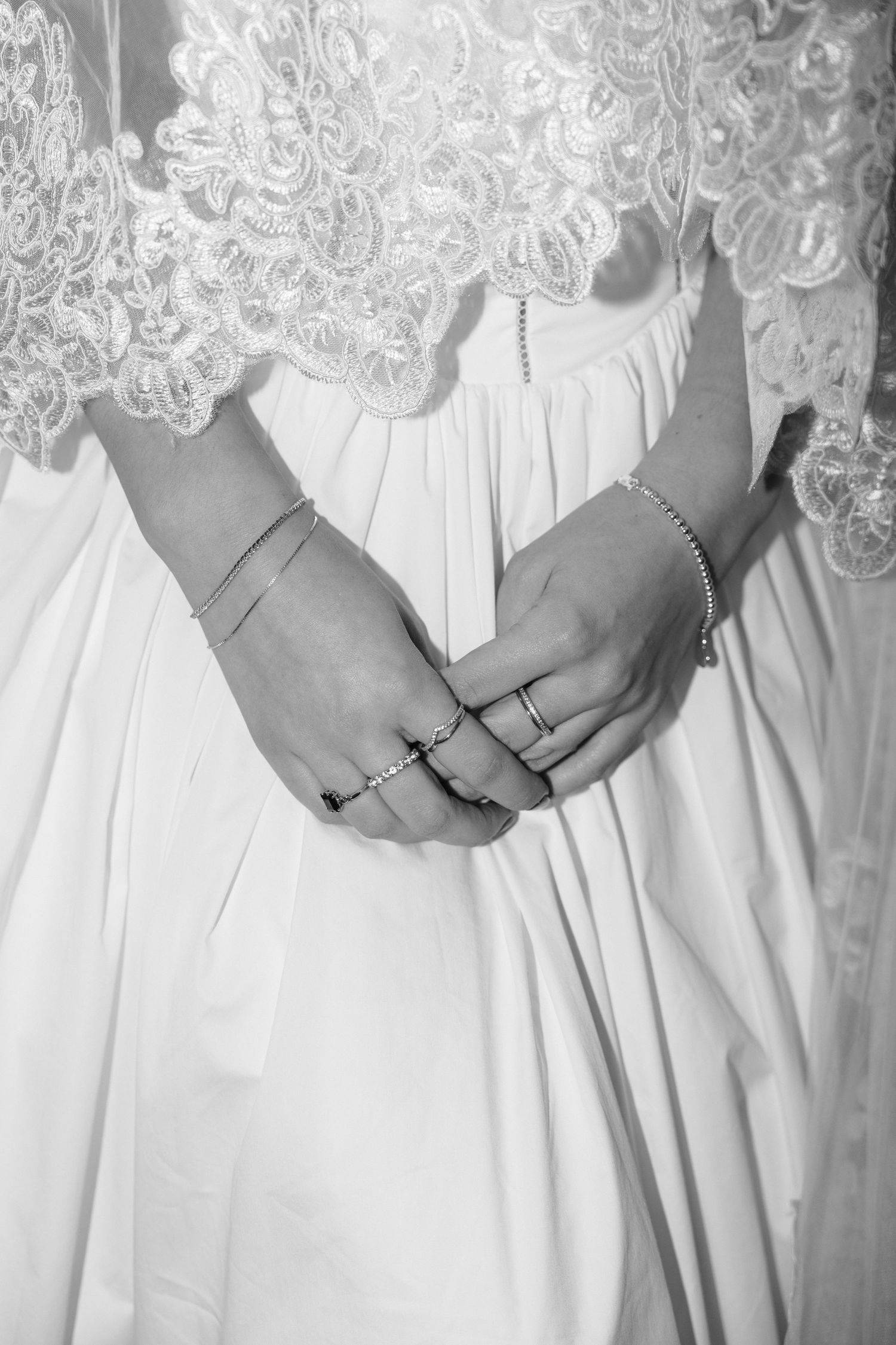 Close-up detail of white lace wedding dress bodice with hands showing multiple rings.