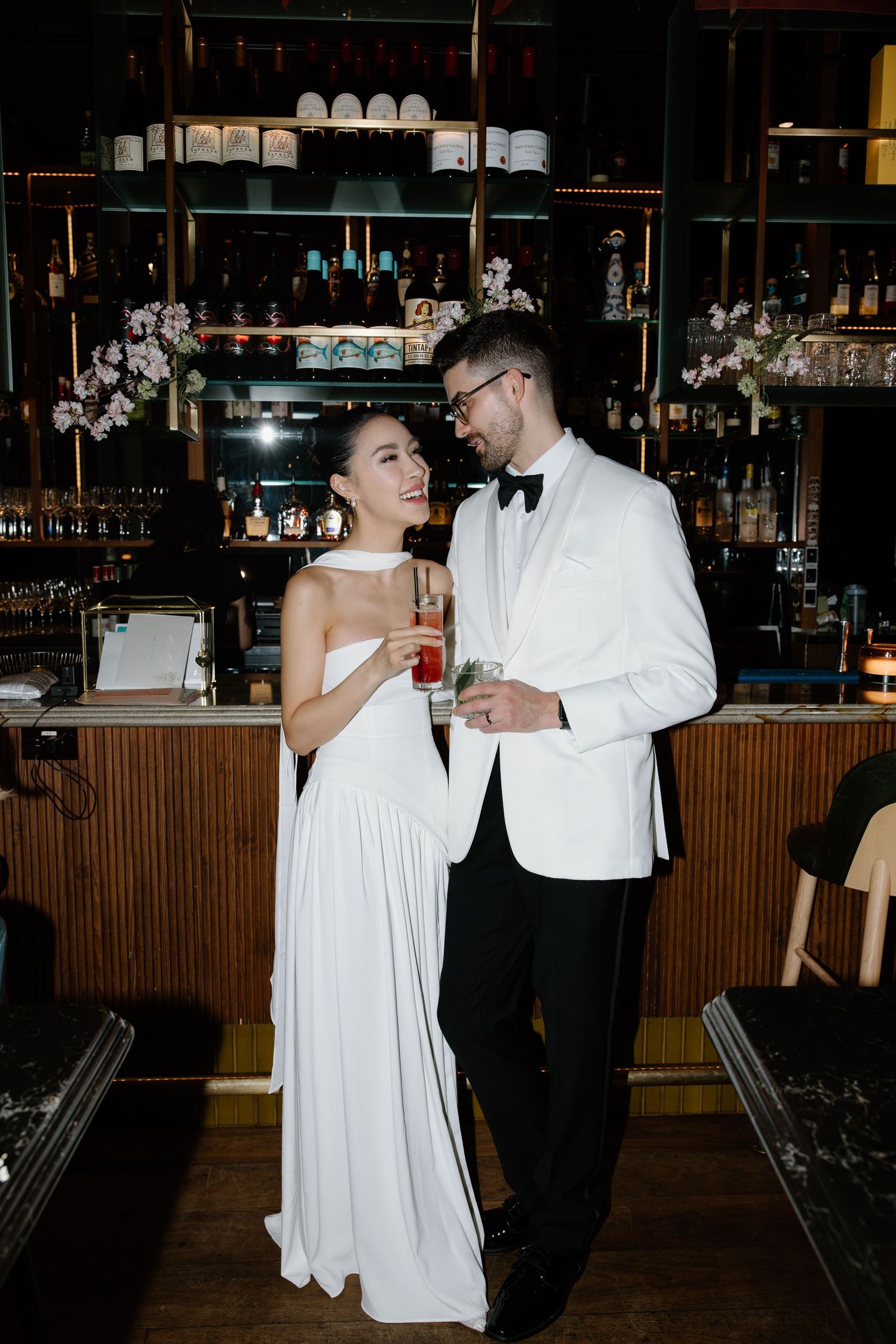 A couple in formal wedding attire dances together at a bar venue with moody lighting.