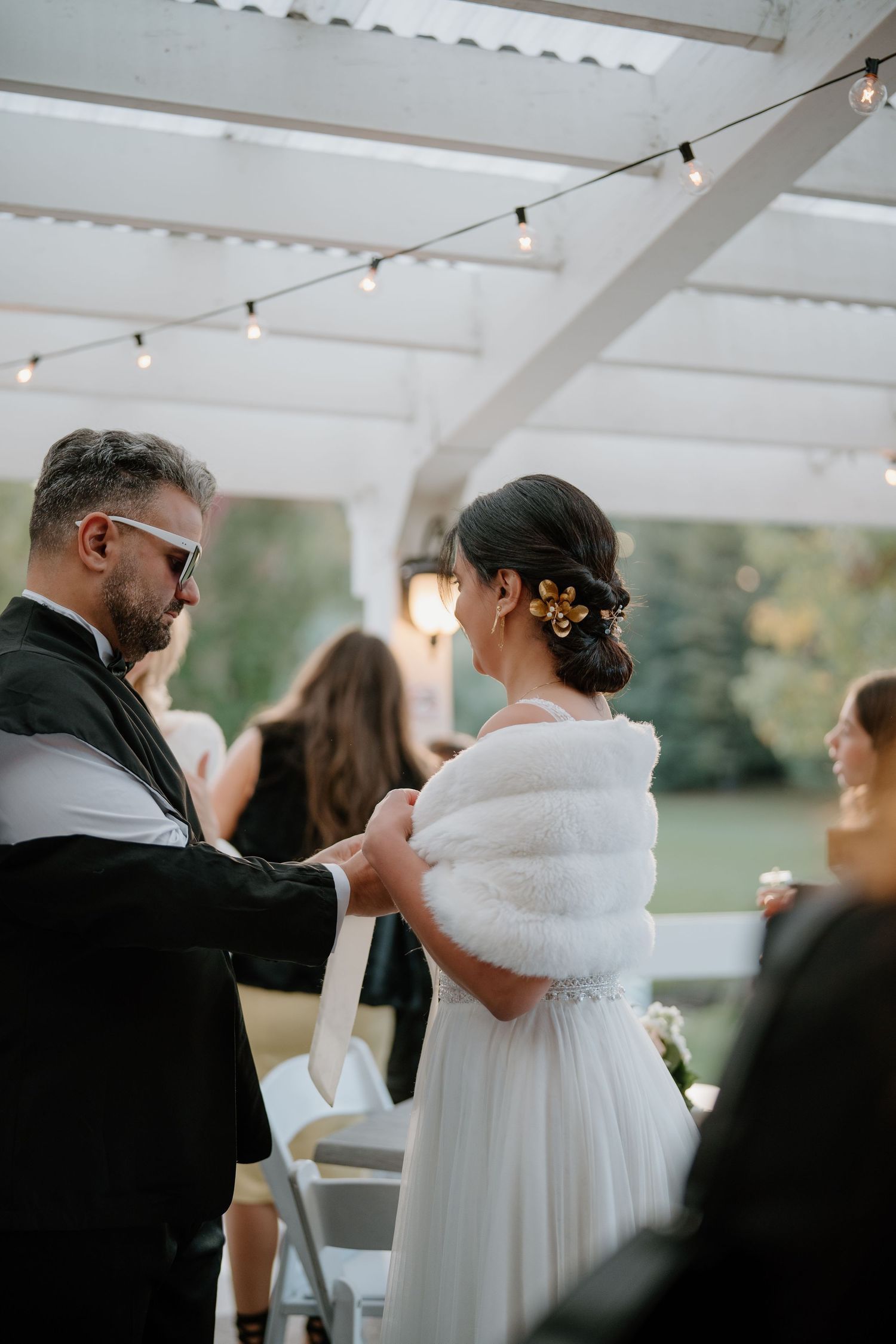 A tender moment between a couple at an outdoor wedding reception with string lights overhead.
