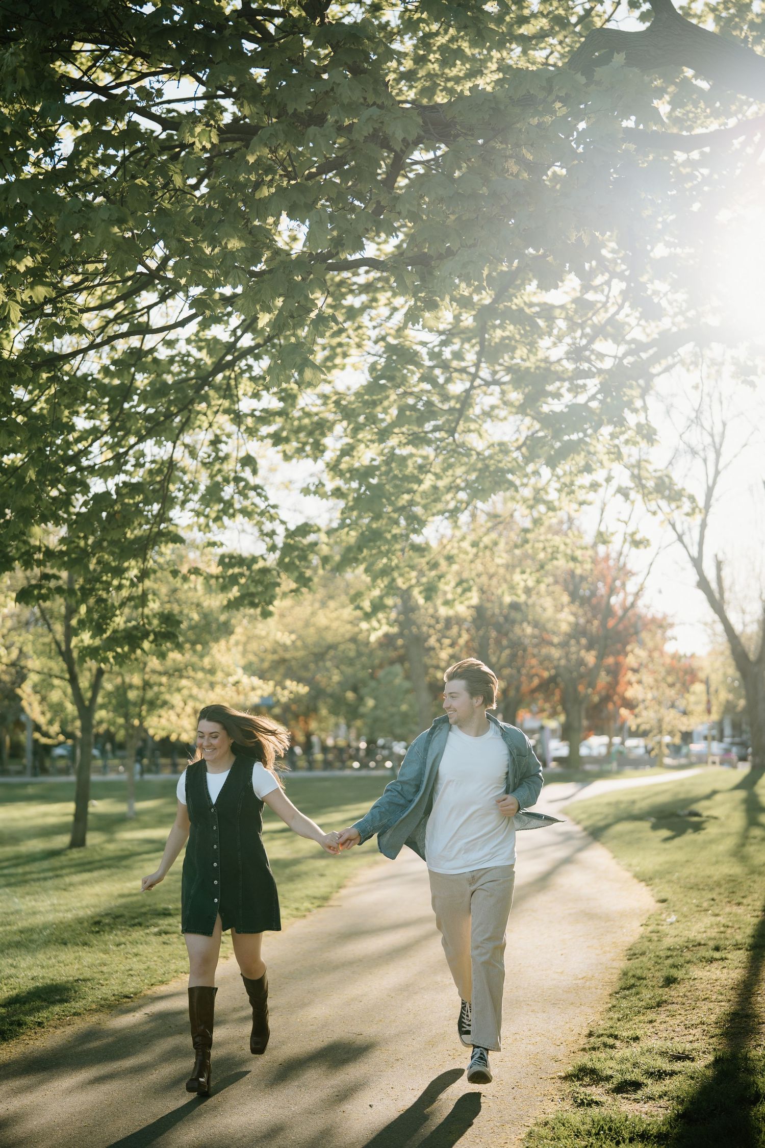 A couple walking together on a tree-lined path in a park during golden hour sunlight.