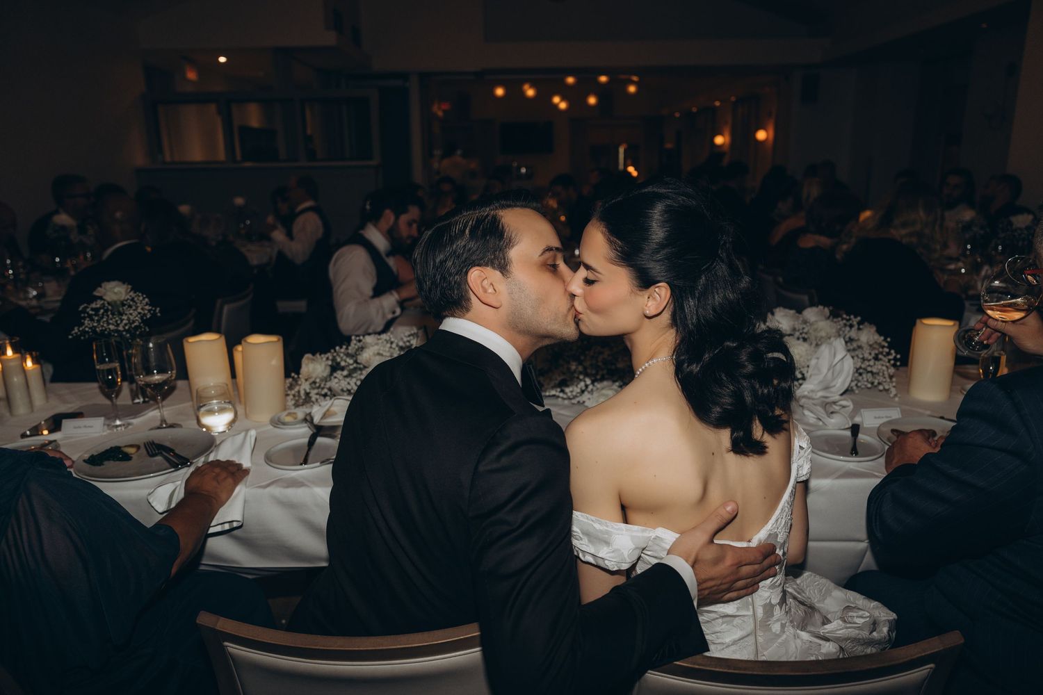 A romantic kiss between a couple at a formal wedding reception in an elegant banquet hall.