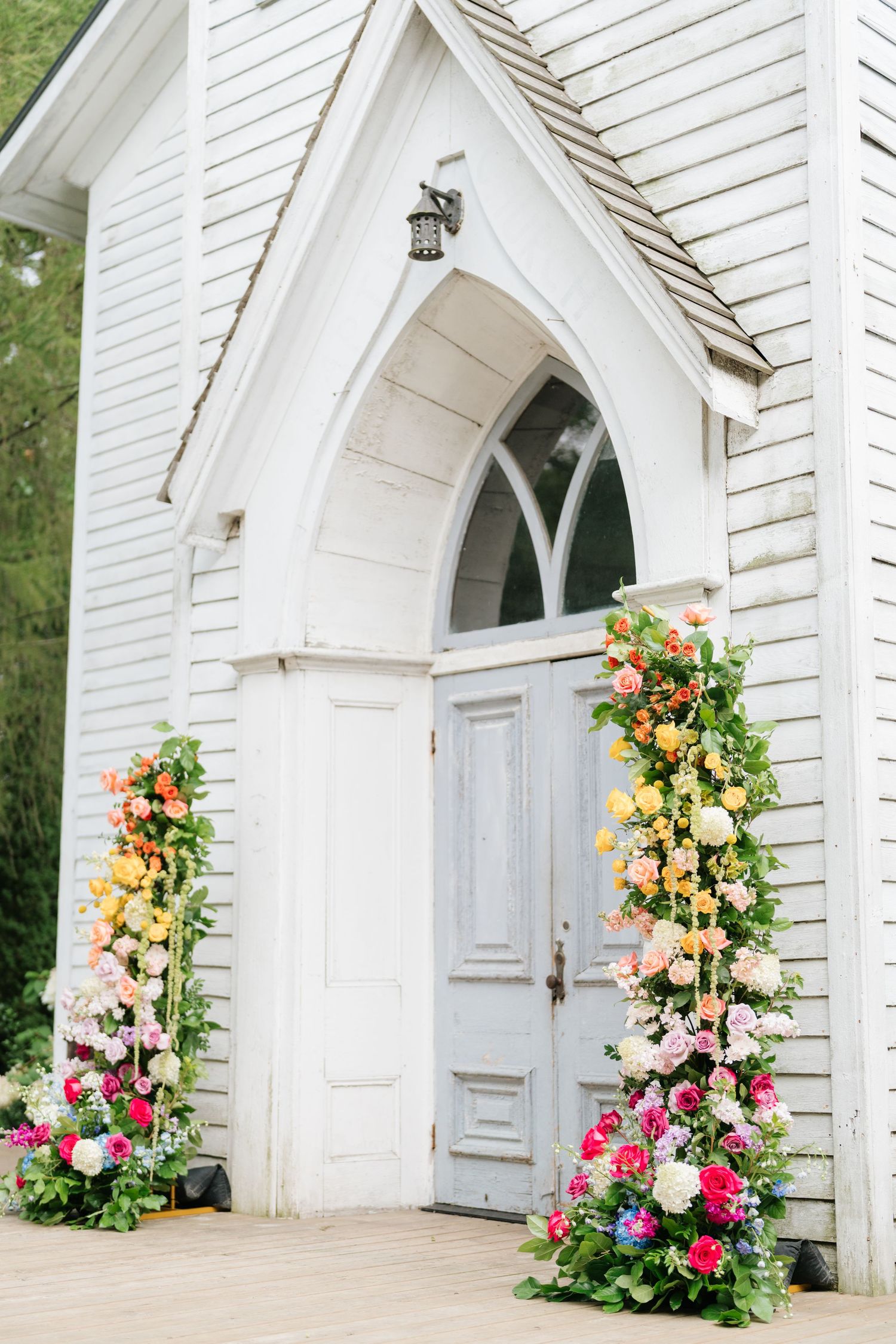 Colorful floral arrangements adorning the white arched entrance of a chapel.