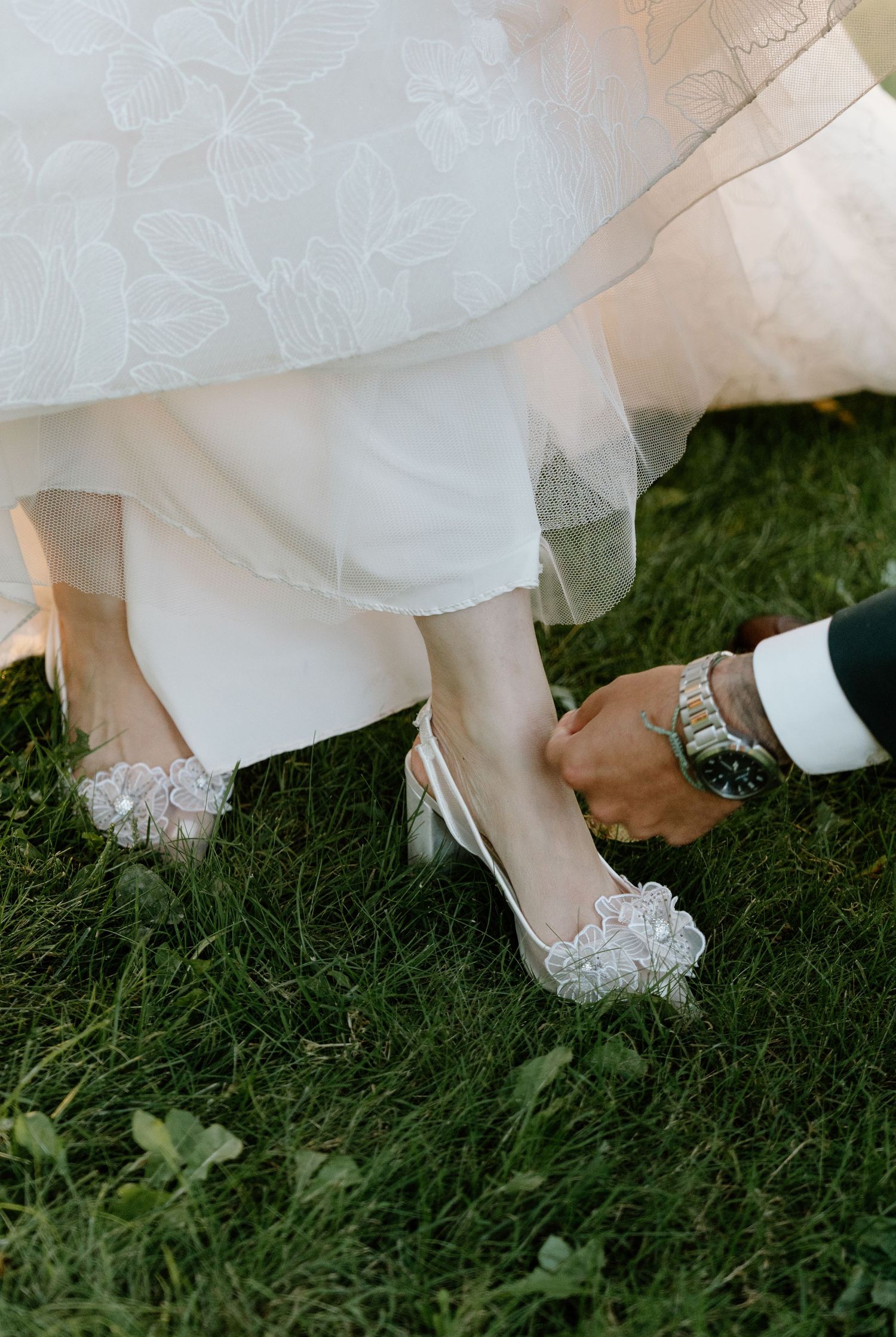 A sequence of photos showing white wedding shoes with floral details being put on while standing on grass.