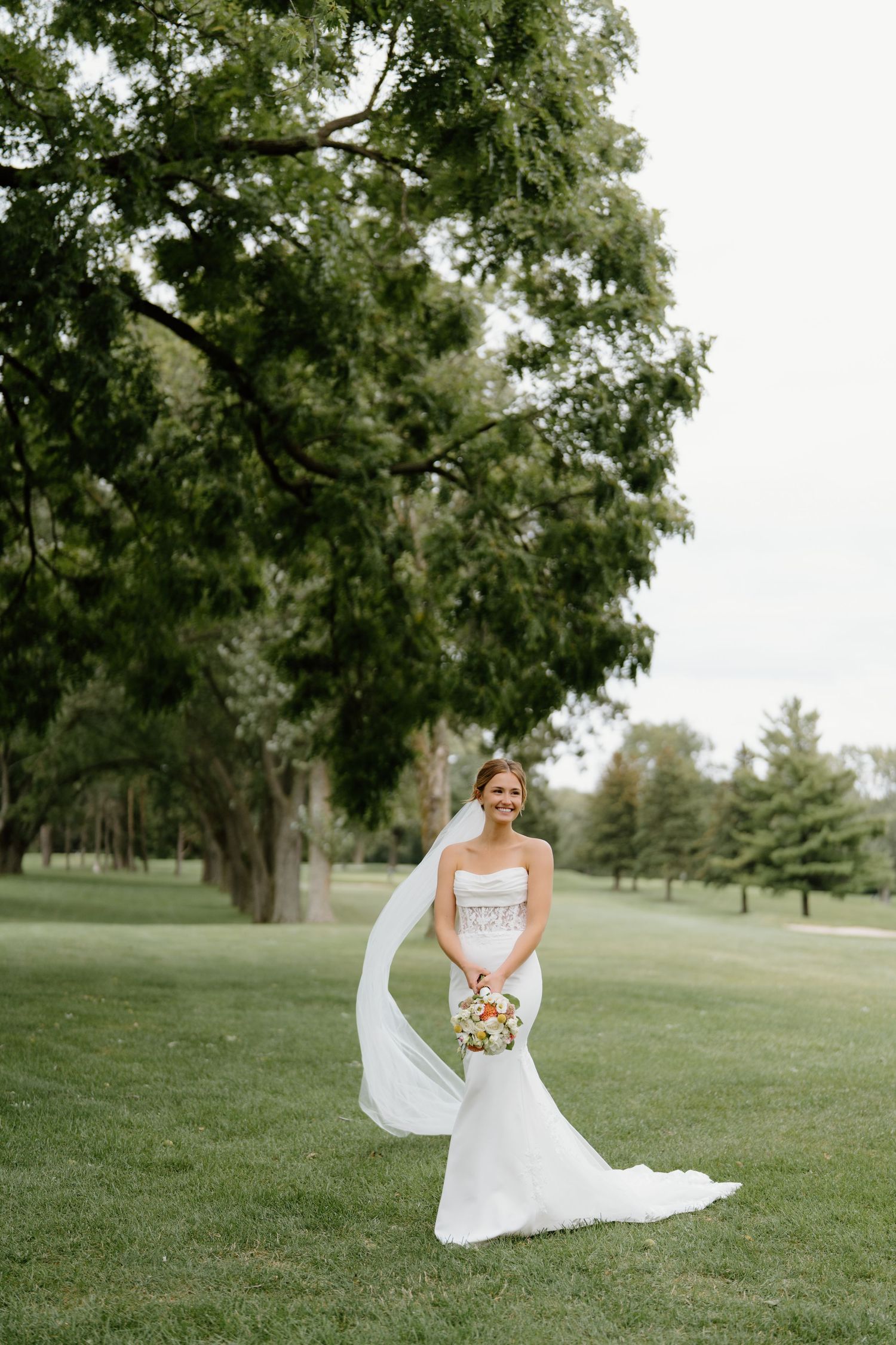 A flowing white wedding dress with a long veil creates an ethereal scene on a lush green lawn.