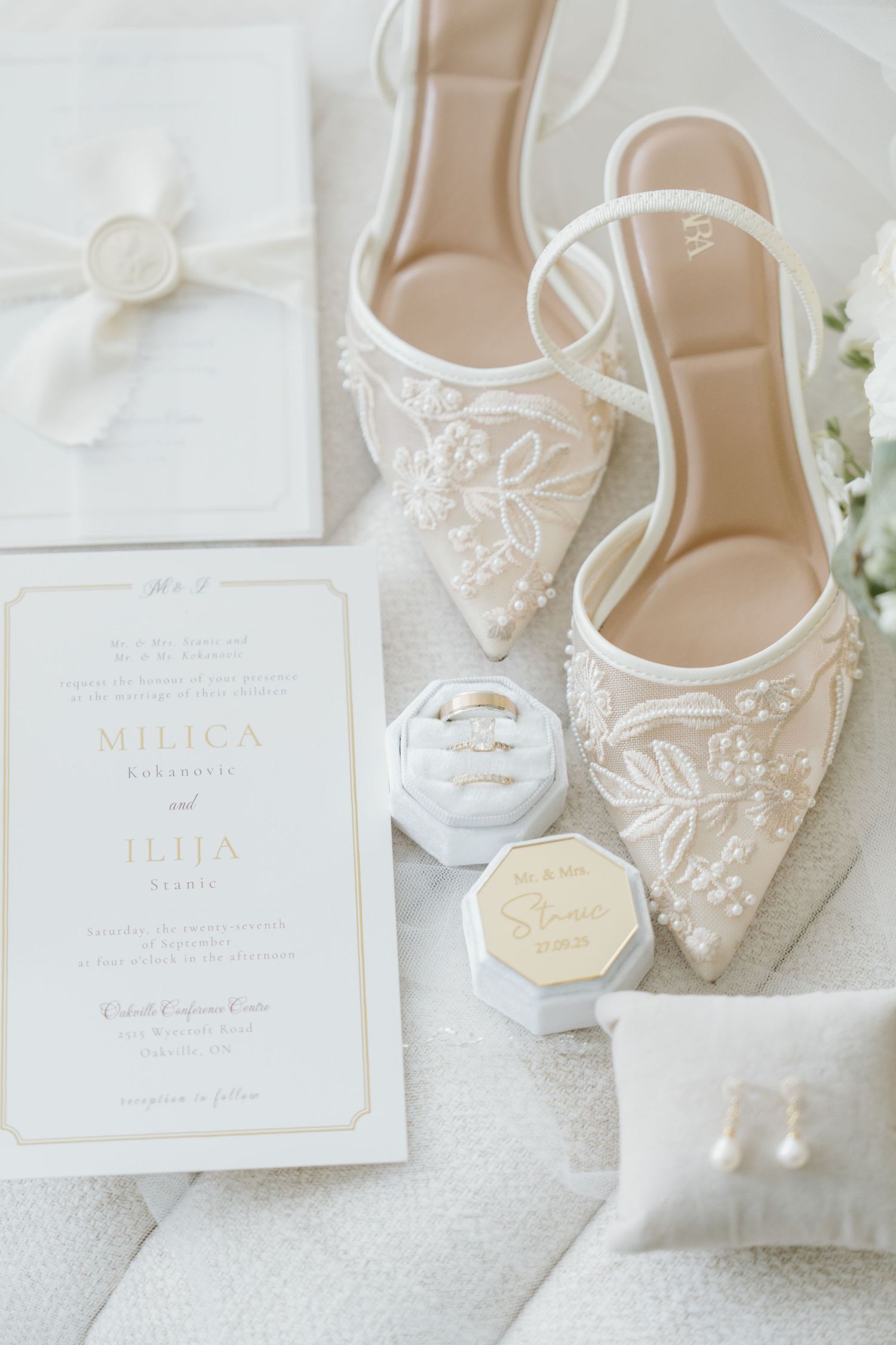 Elegant bridal shoes with delicate lace details displayed alongside white wedding invitations and floral accents.