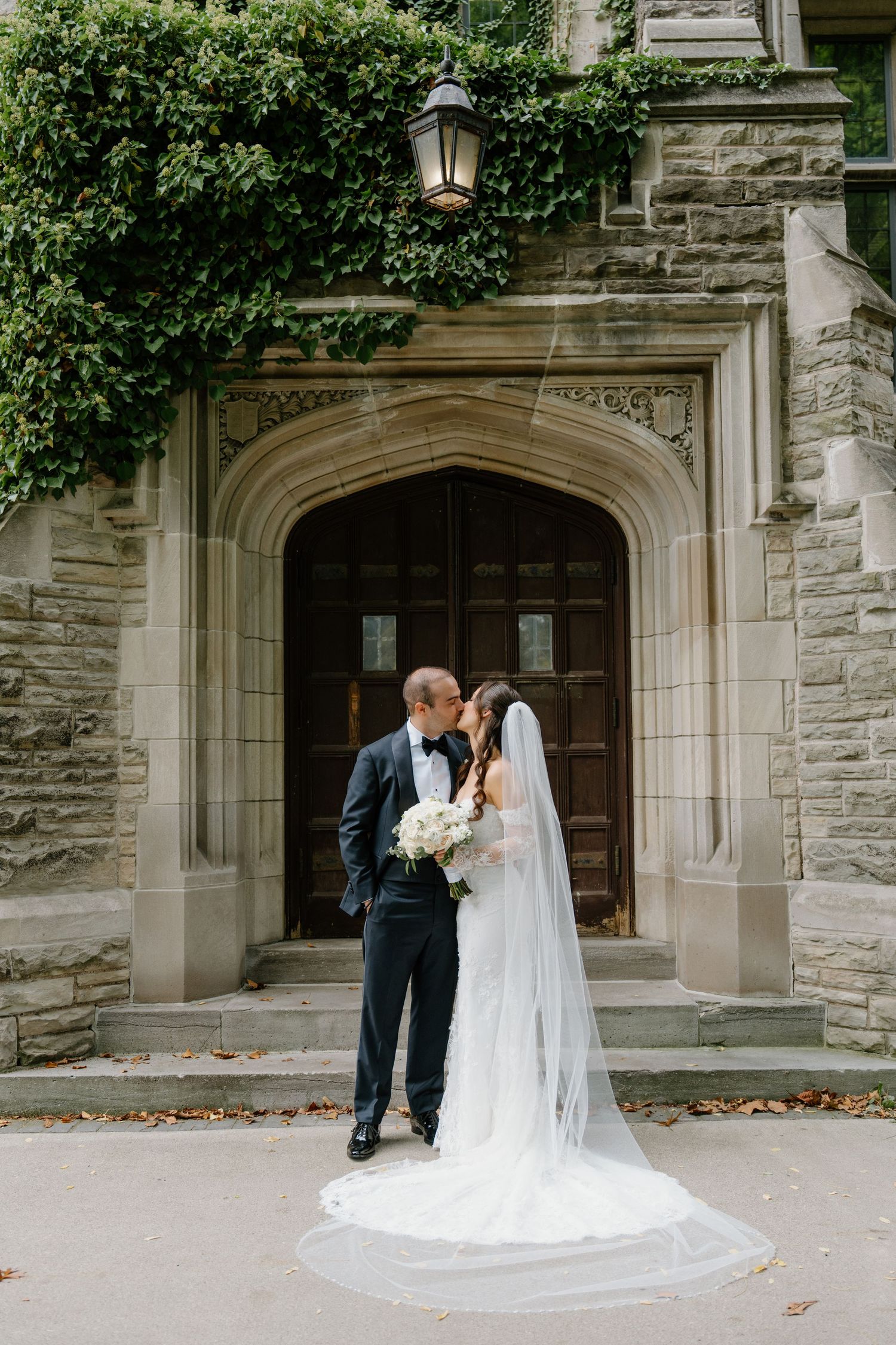 A couple shares romantic wedding moments in front of a grand stone church entrance with ivy-covered walls.