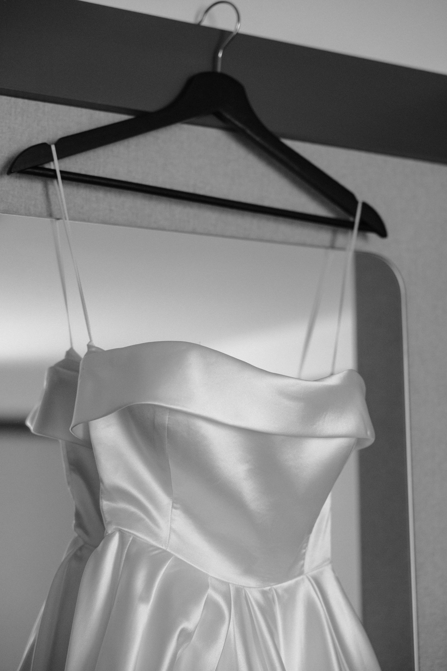 A white satin wedding dress bodice with strapless sweetheart neckline hanging on a black hanger against a wall.