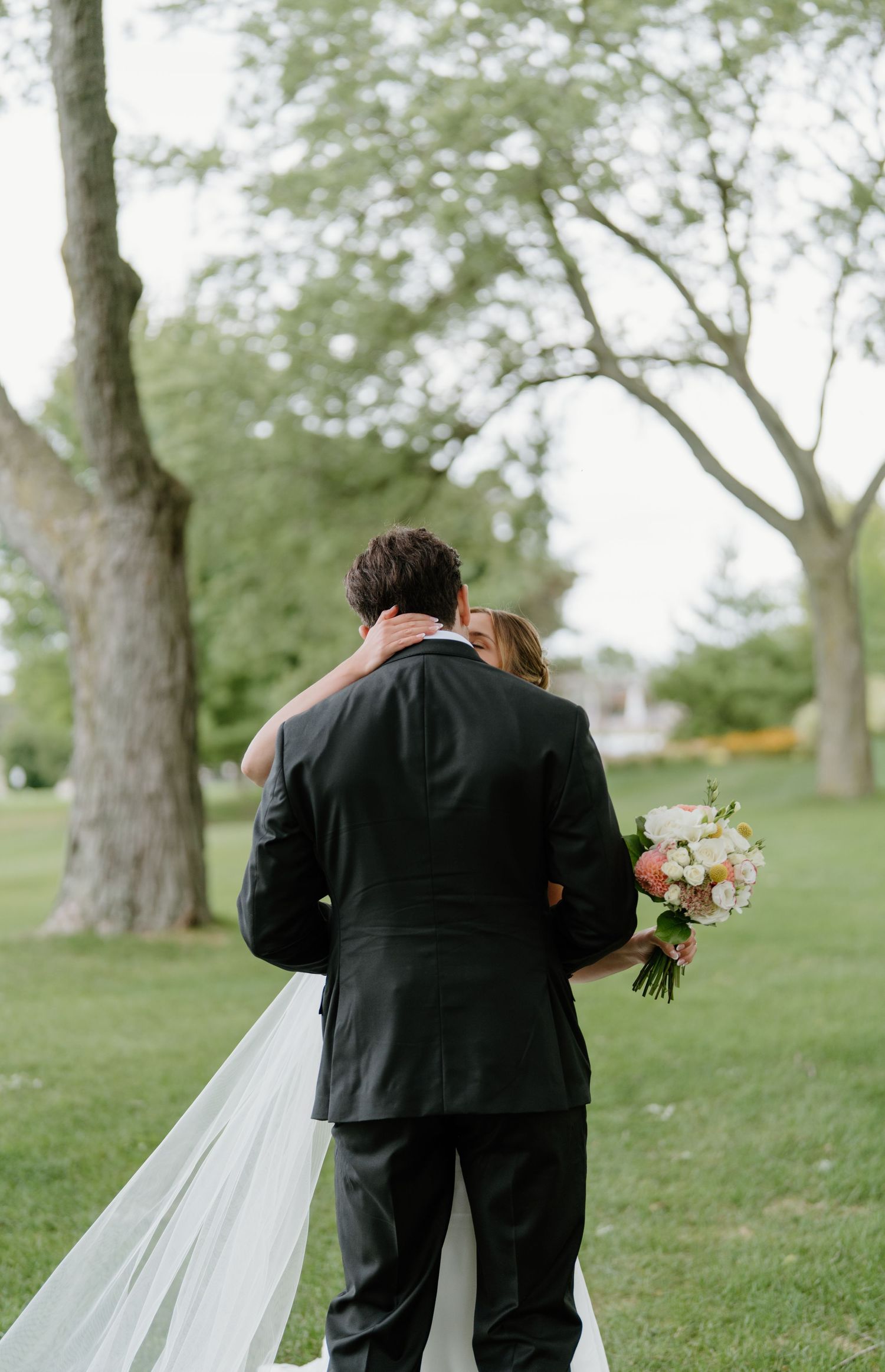 Newlywed couple walking together through a scenic park setting with trees and grass.