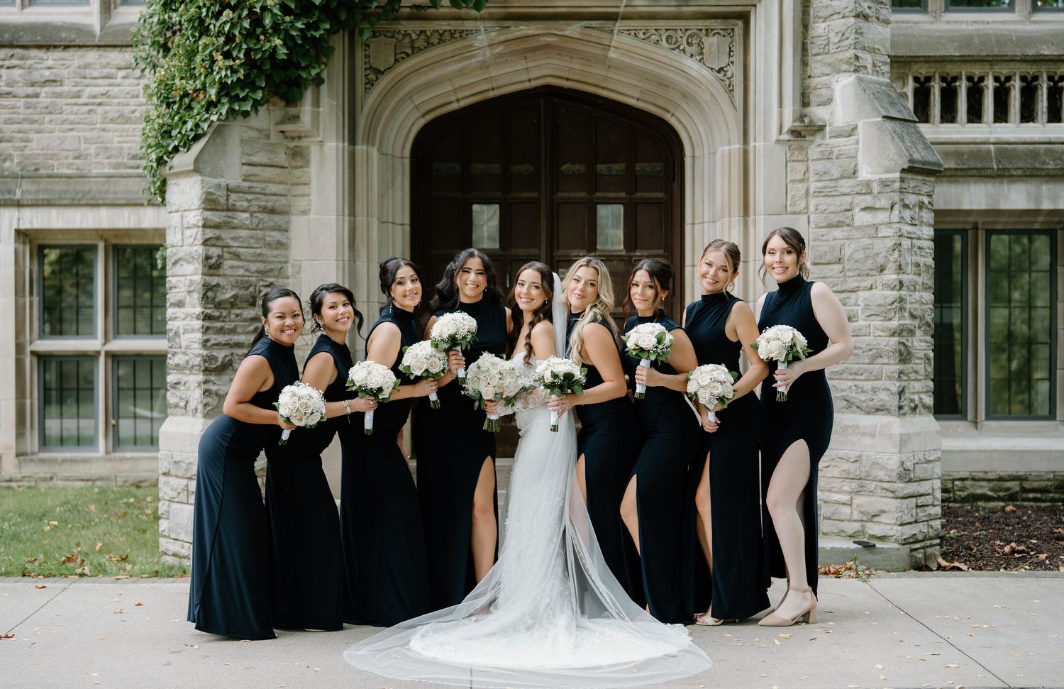 Wedding party gathers on stone steps of historic building for formal group photo.