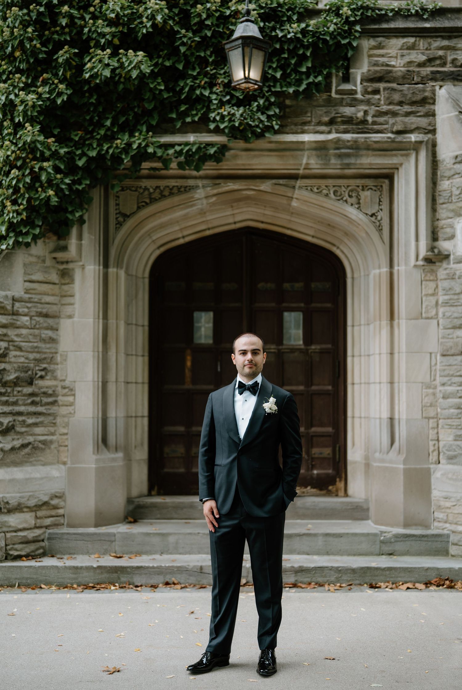 A formal portrait of a groom in front of an elegant stone archway entrance.