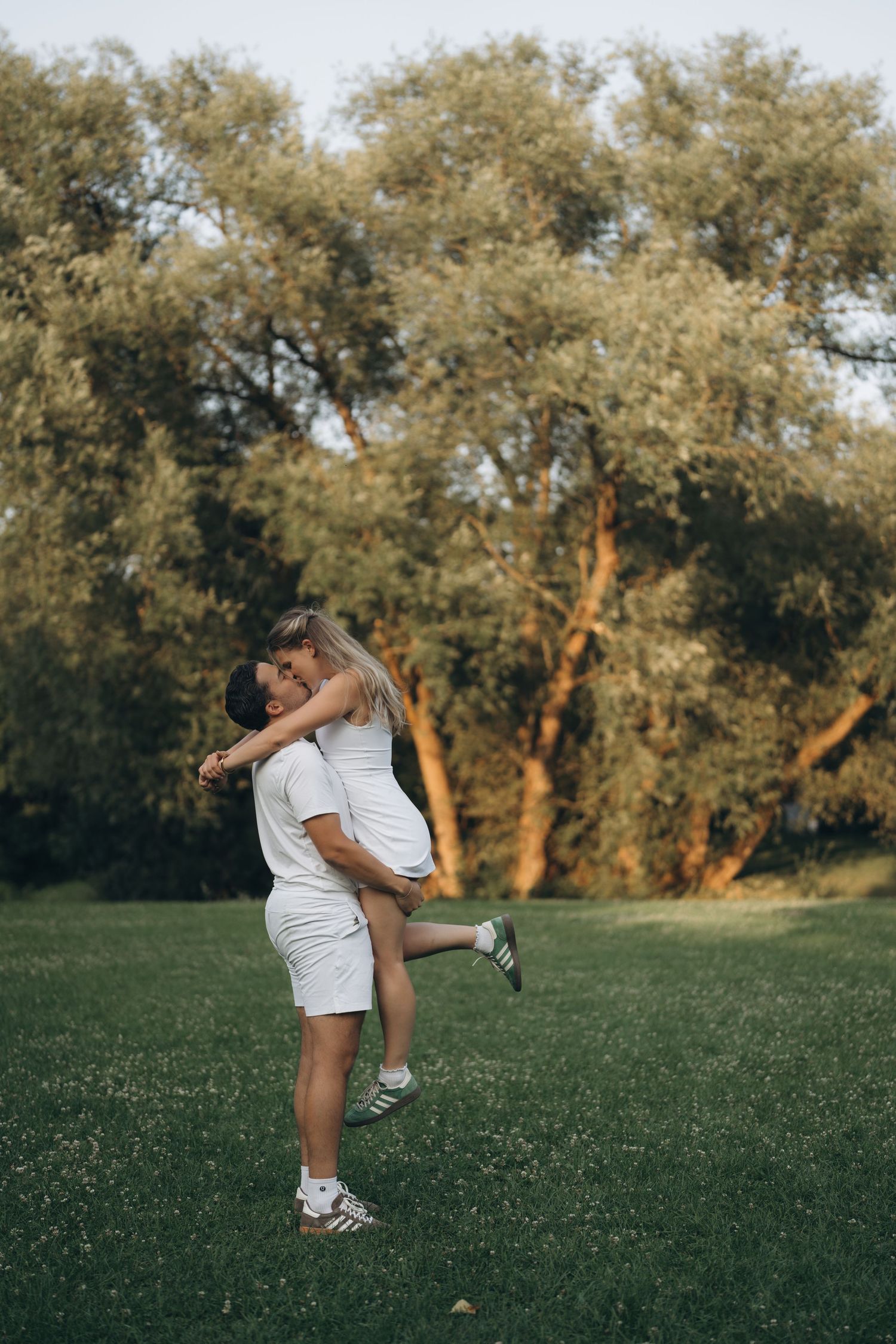 Person demonstrates stretching exercises on a grassy lawn at sunset with trees in the background.