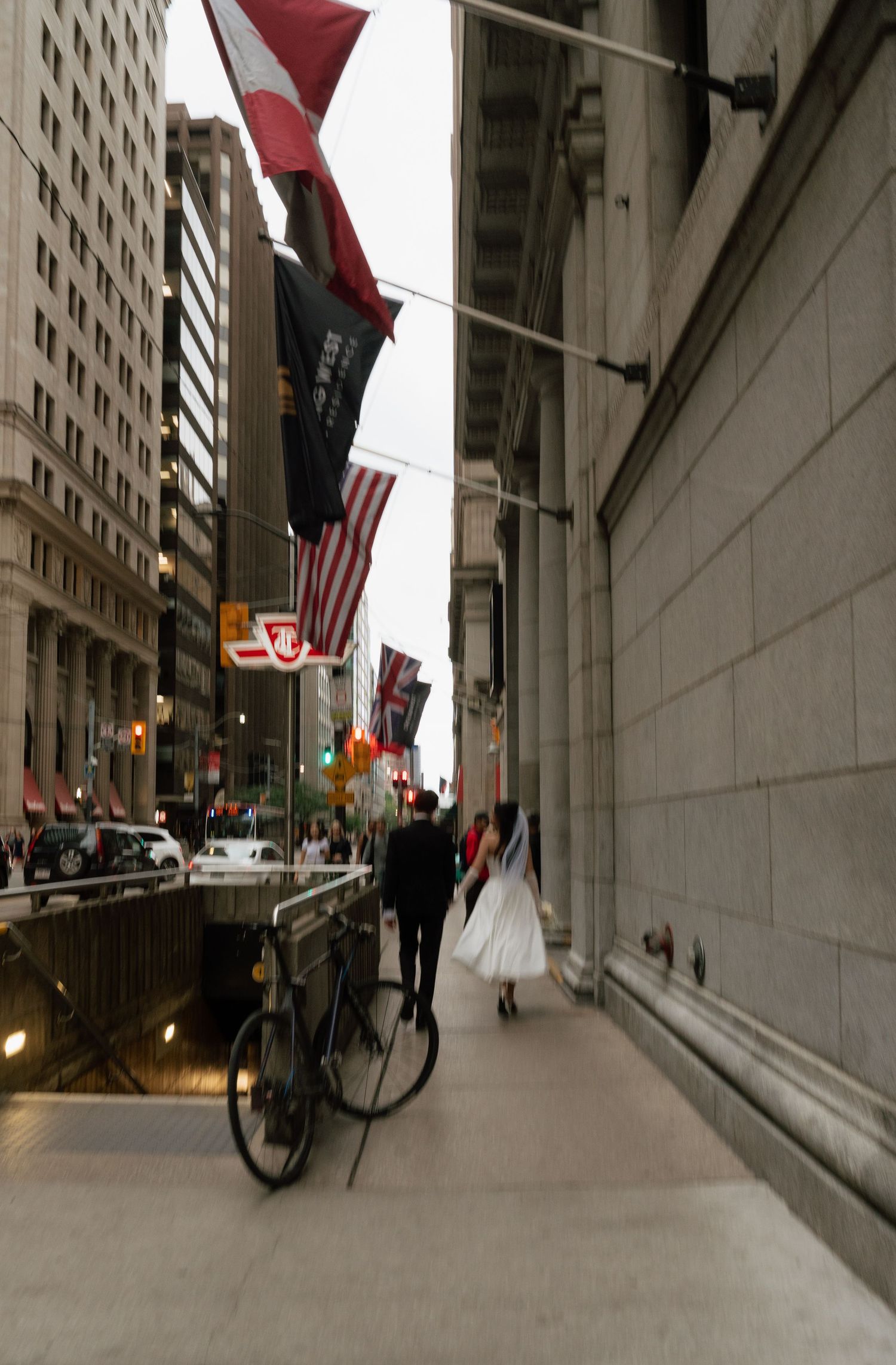 Urban street scene with American flags and red banners mounted on a stone building in a downtown setting.