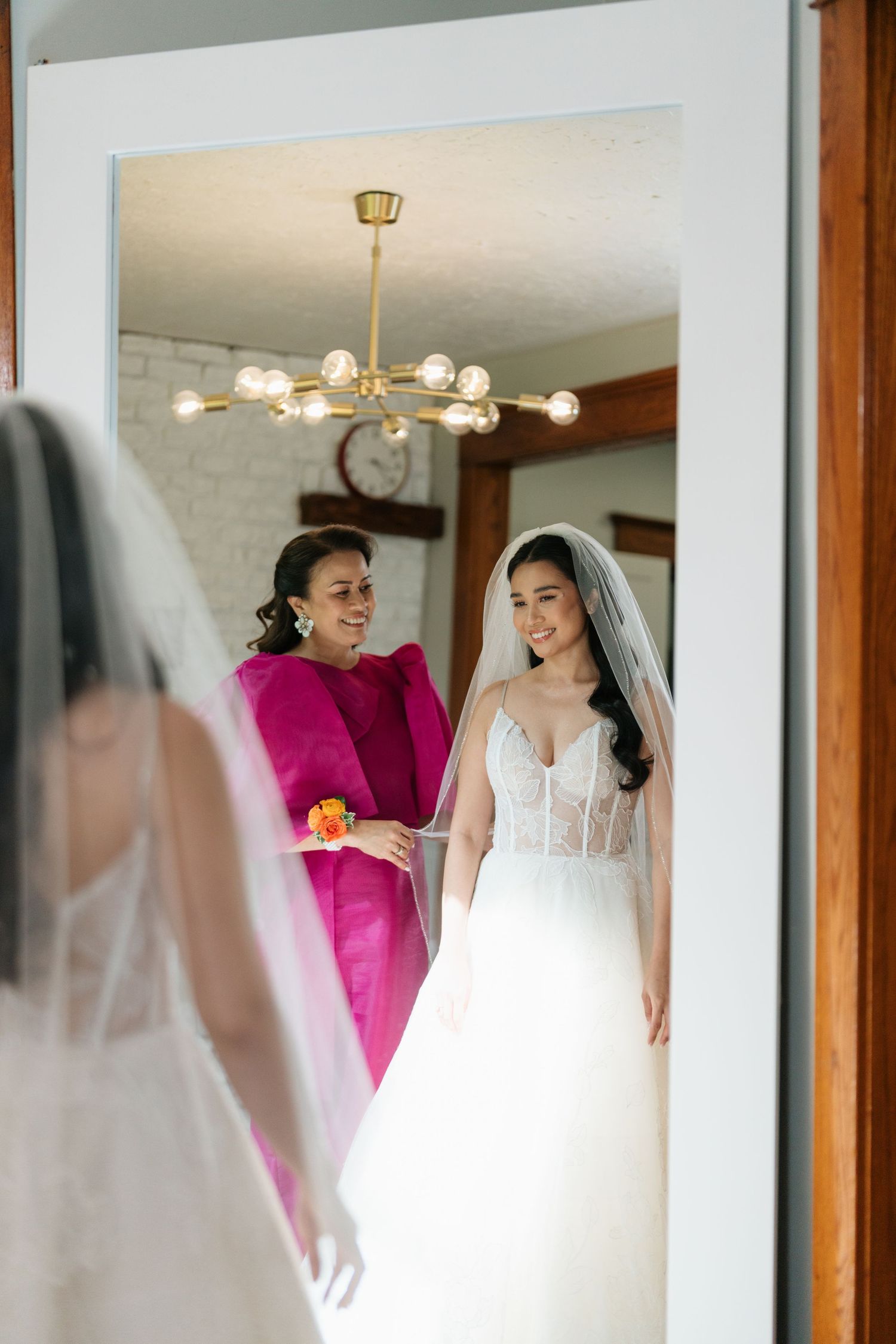 A bride in a white wedding dress is reflected multiple times in mirrored closet doors during wedding preparations.