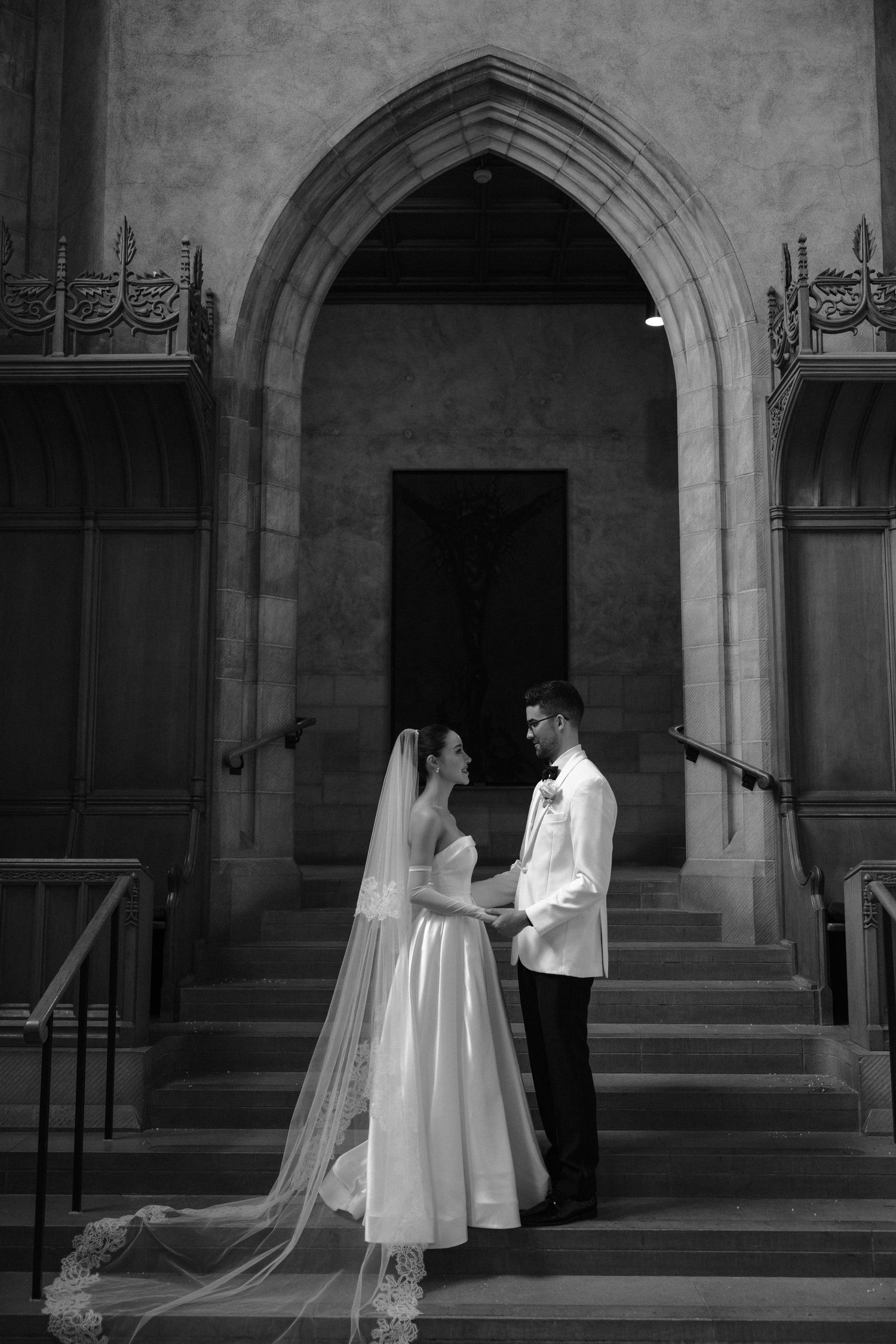 A black and white wedding photo series showing a couple in formal attire against an archway entrance of a stone building.