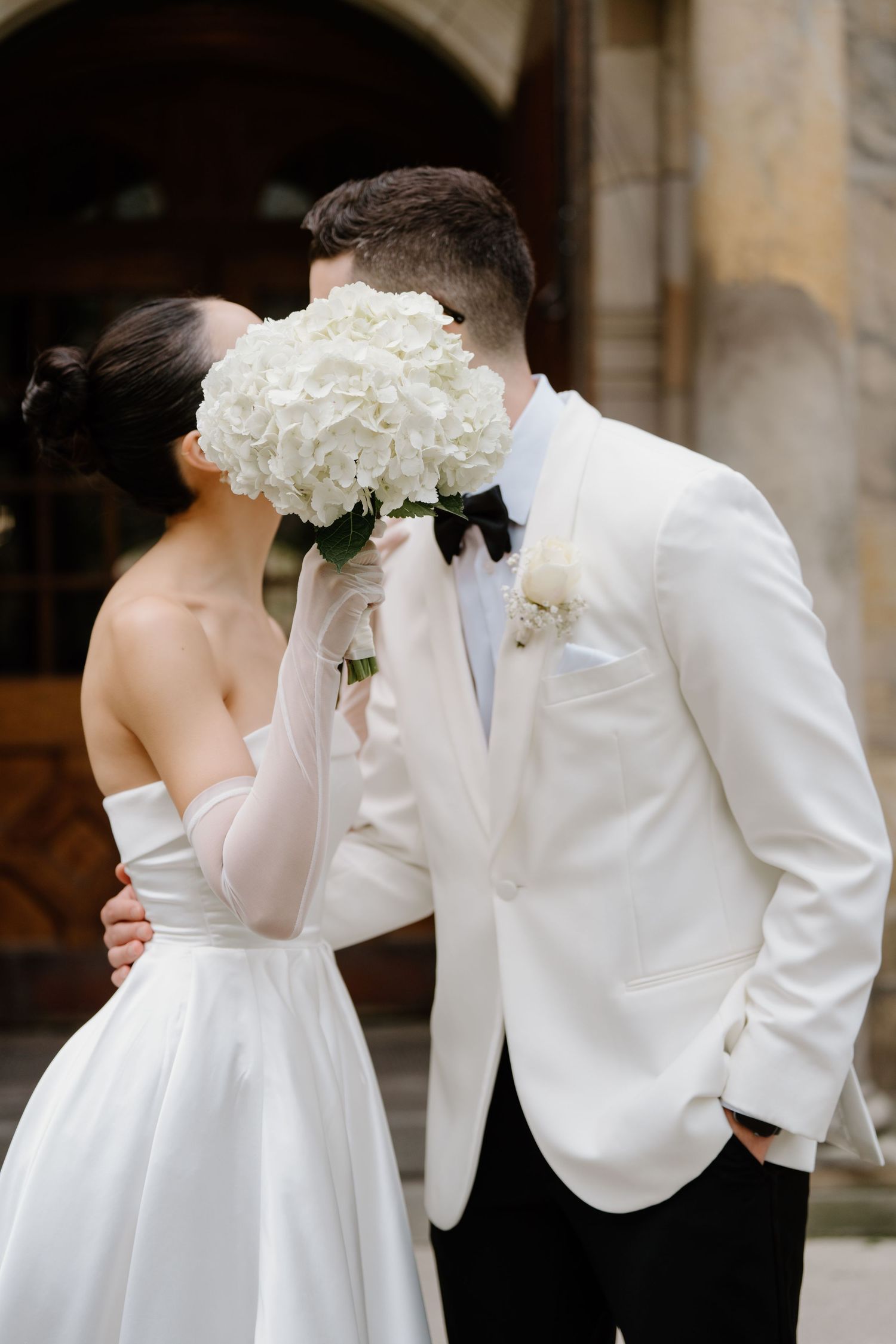 A couple embraces on their wedding day with a white hydrangea bouquet perfectly placed between them.