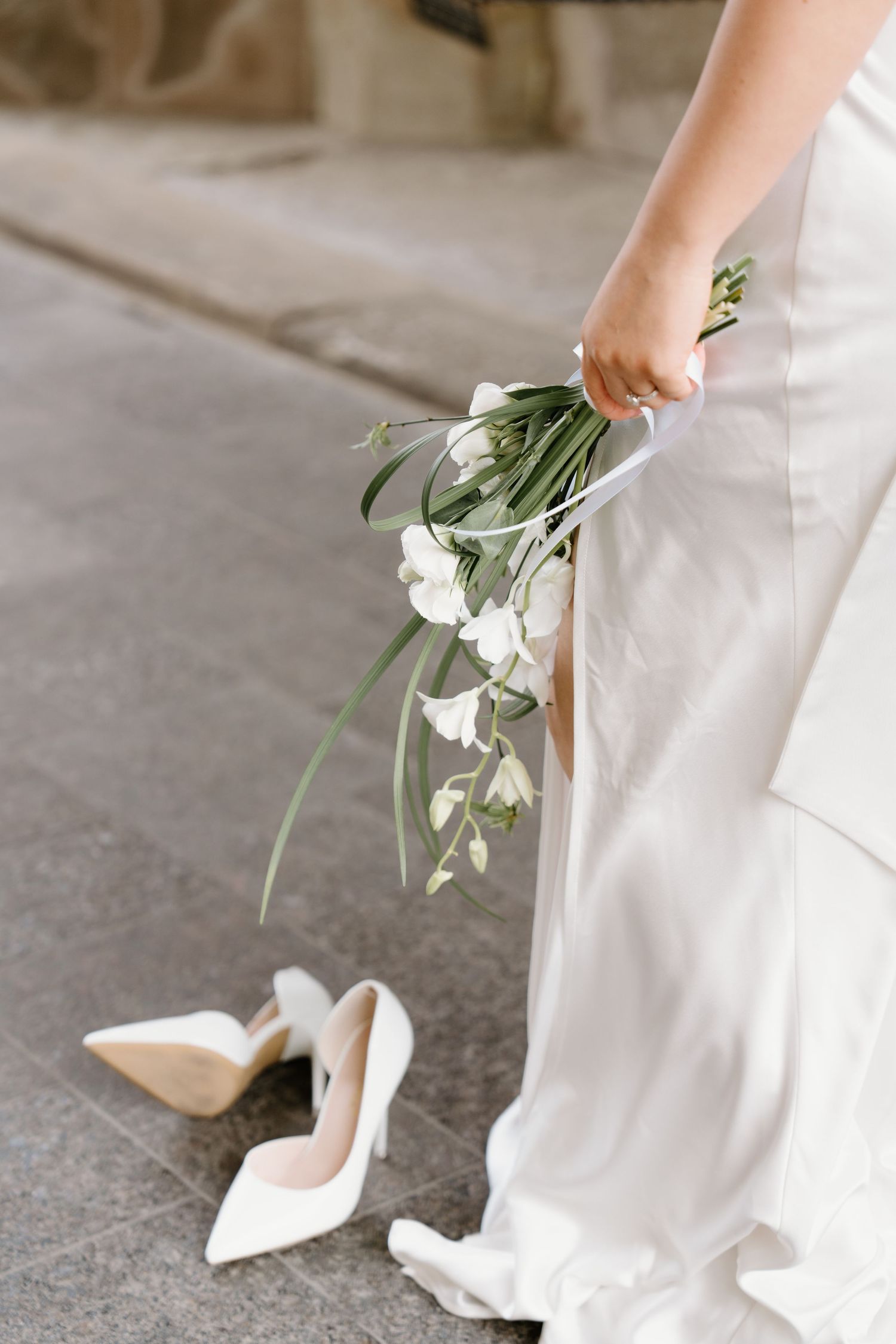 A bride in a white wedding dress holding a delicate bouquet, showing elegant shoes and flowing gown details.