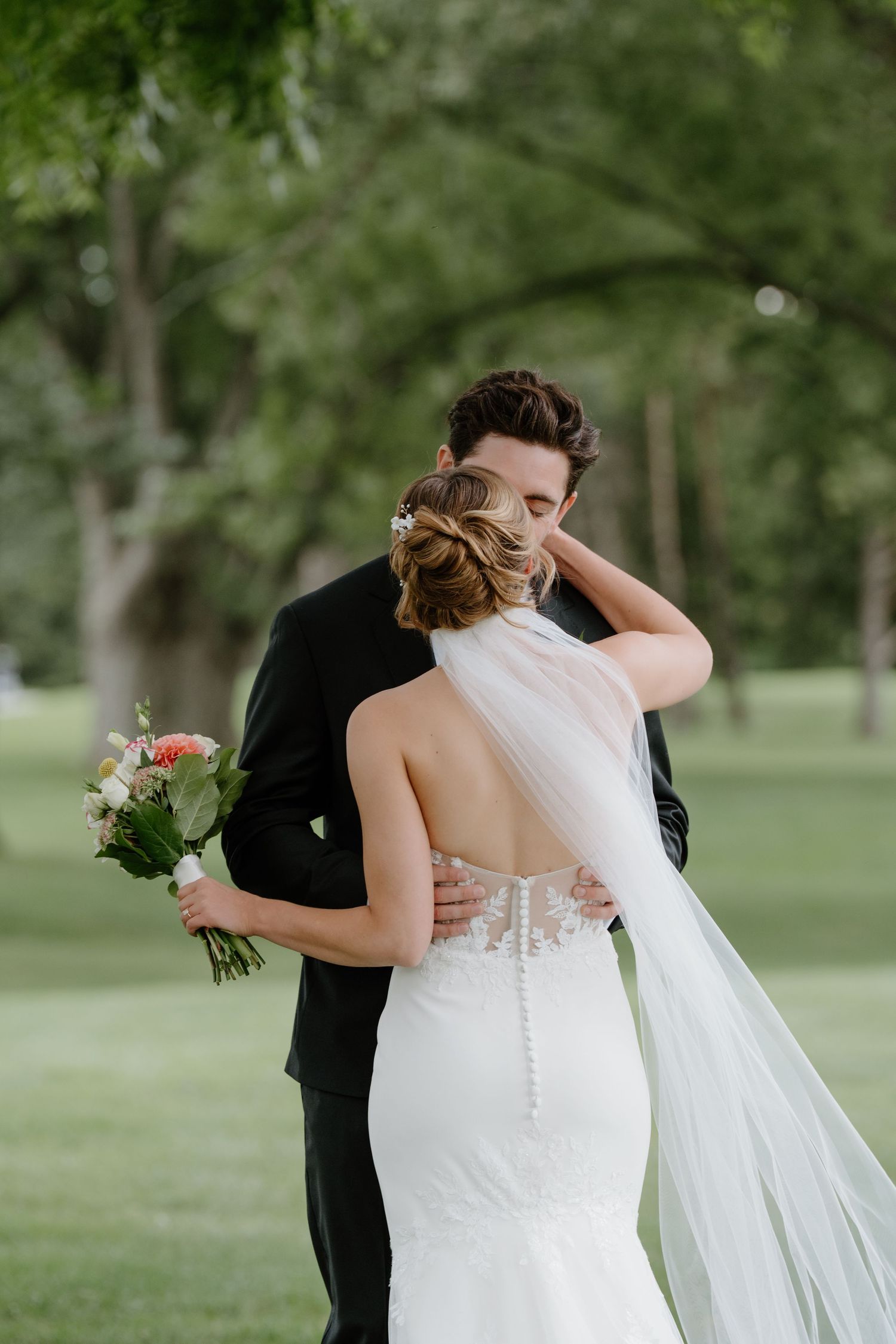 A romantic first look moment between newlyweds embracing in a lush green garden setting.