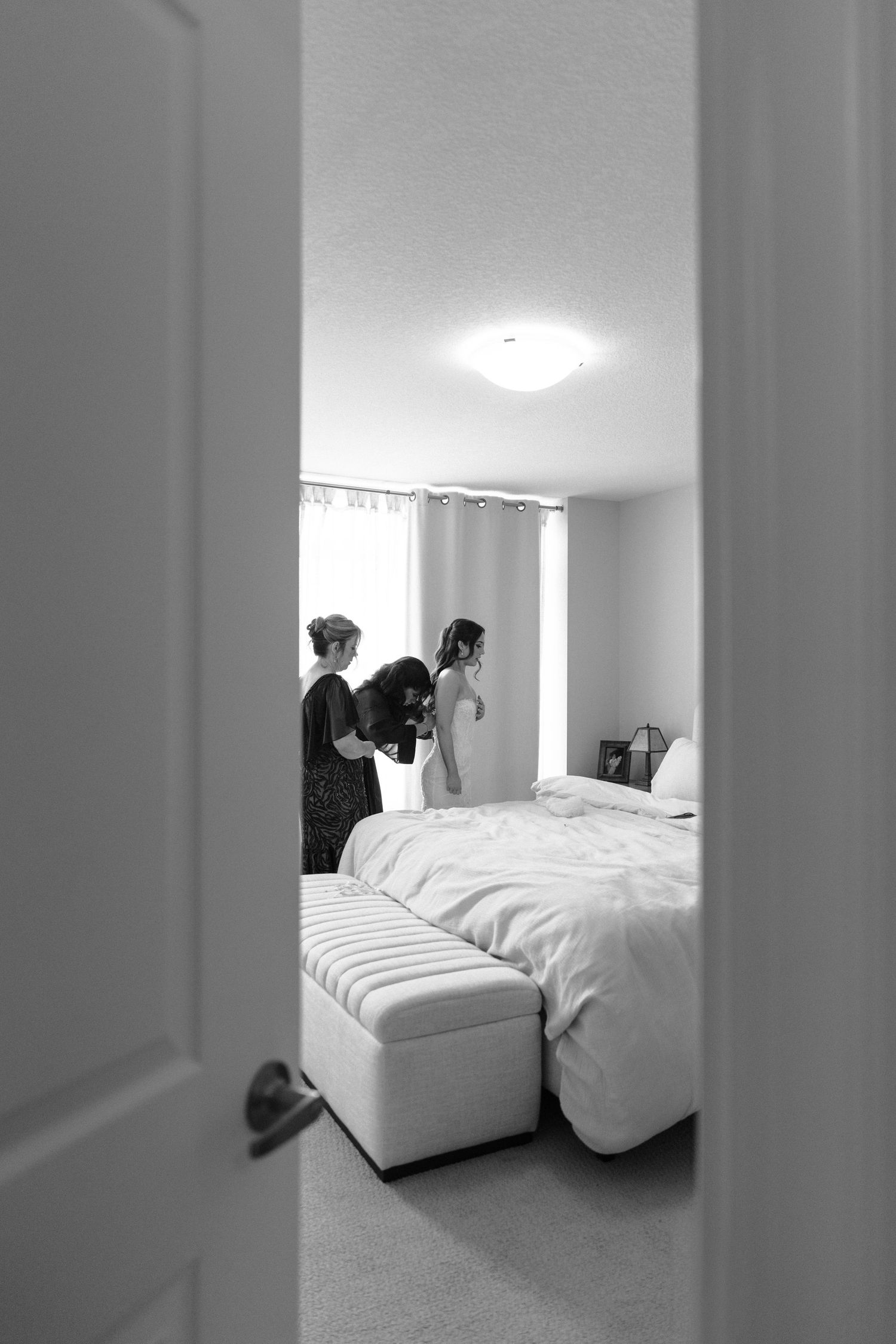 A minimalist bedroom interior with white bedding viewed through a doorway in black and white photography.