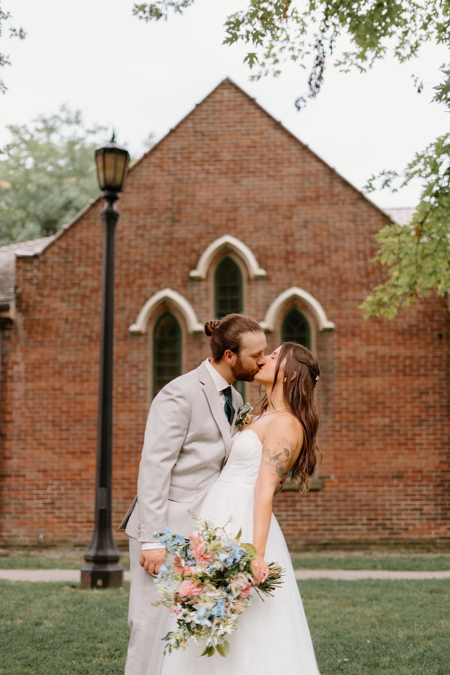 A romantic wedding moment outside a brick church with Gothic arched windows and a vintage lamp post.