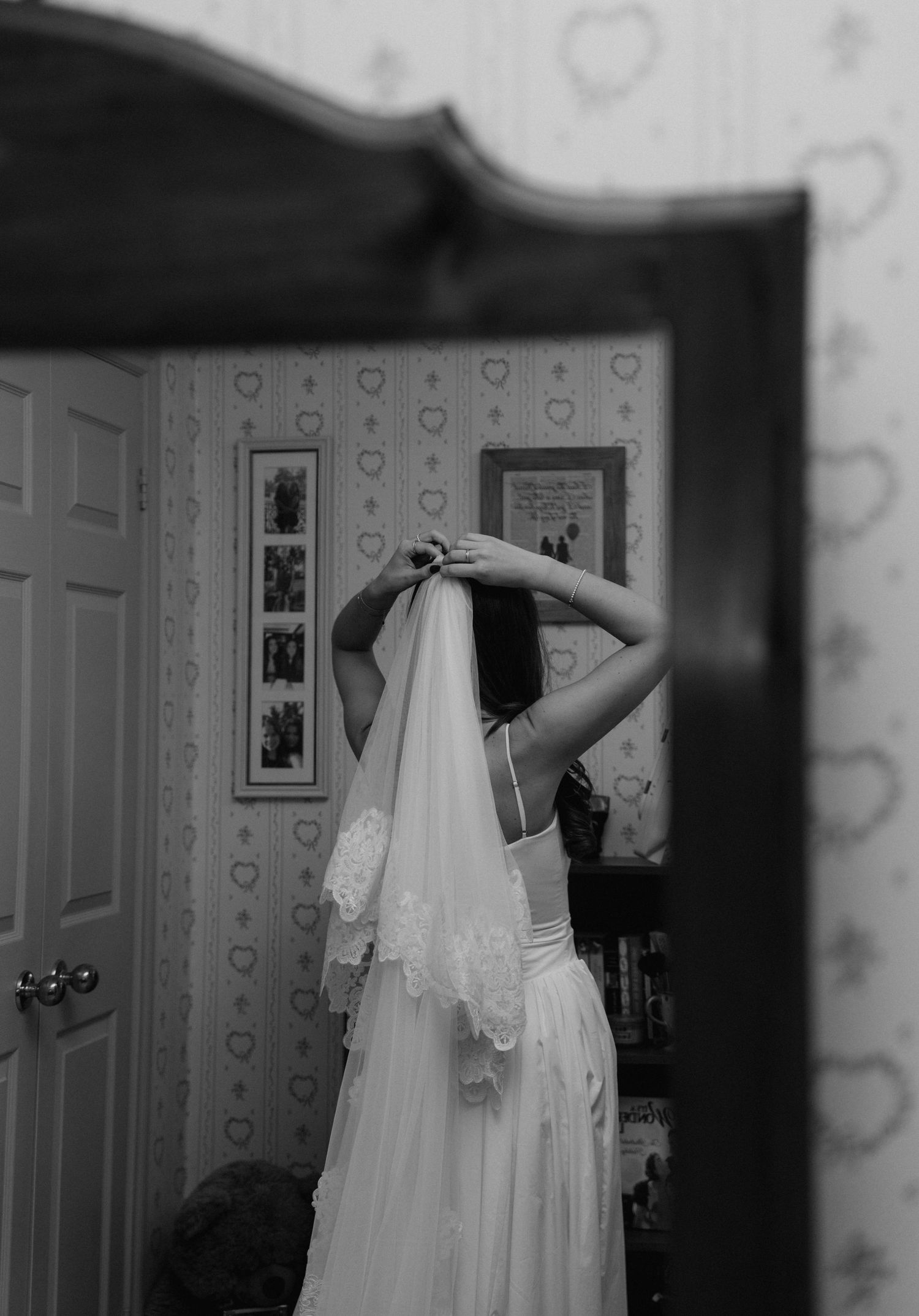 A monochromatic photo series showing a bride getting ready with her delicate lace veil in a bedroom mirror.