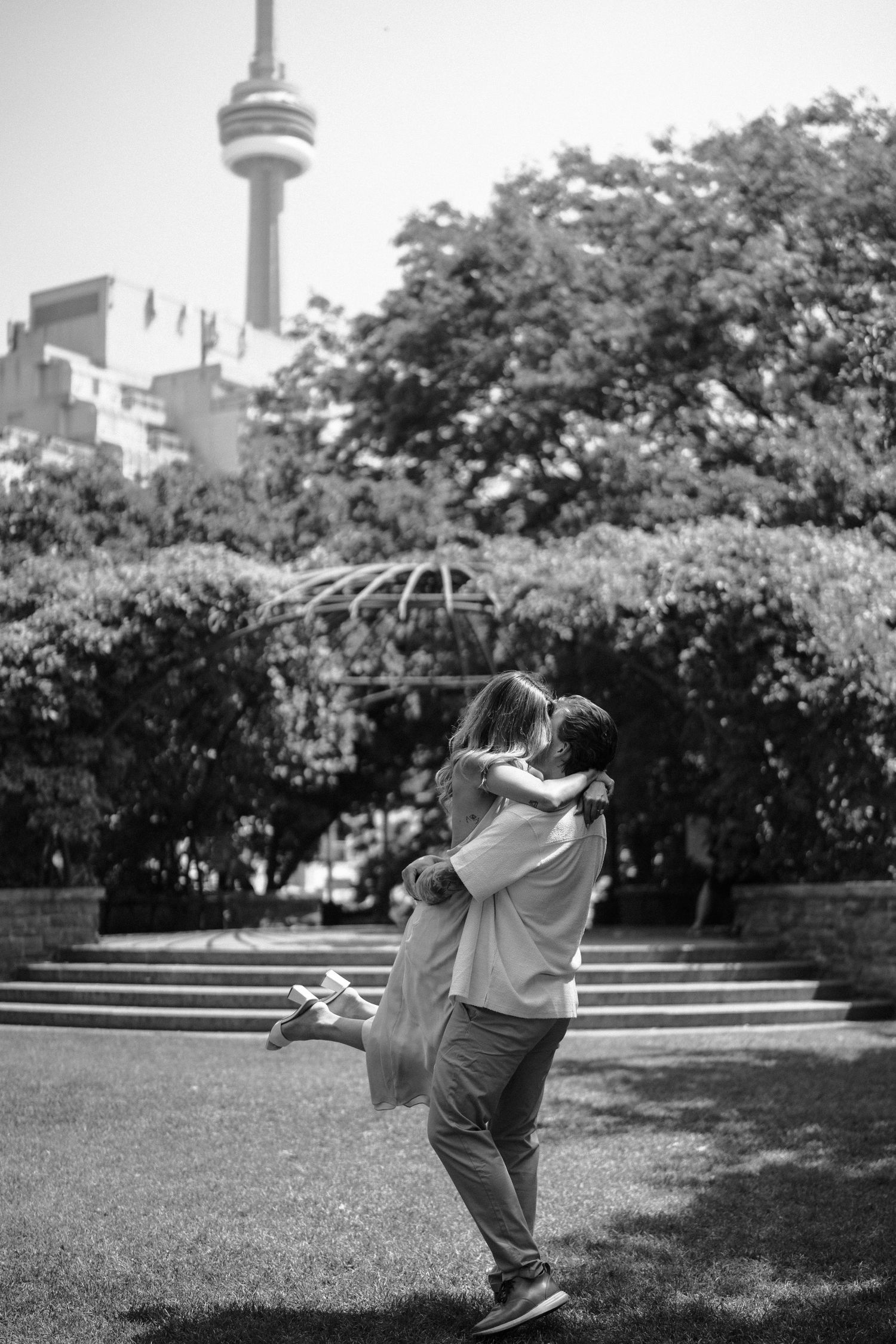 A tender moment captured in black and white as a couple hugs in a Toronto garden with the CN Tower visible.