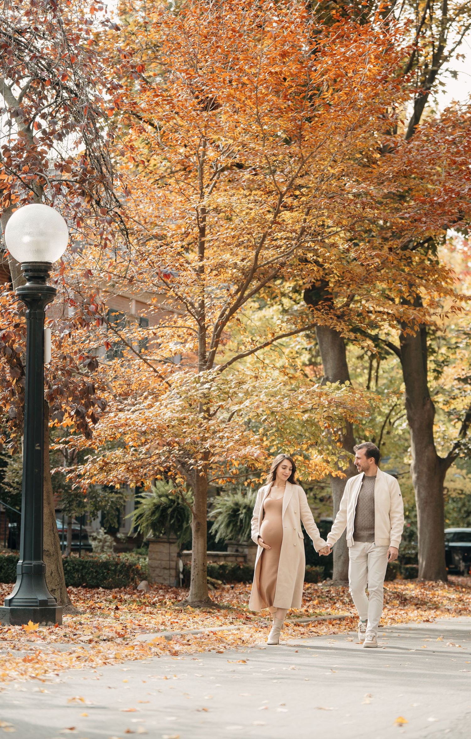 A couple strolls down a path under vibrant orange autumn trees on a romantic fall afternoon.
