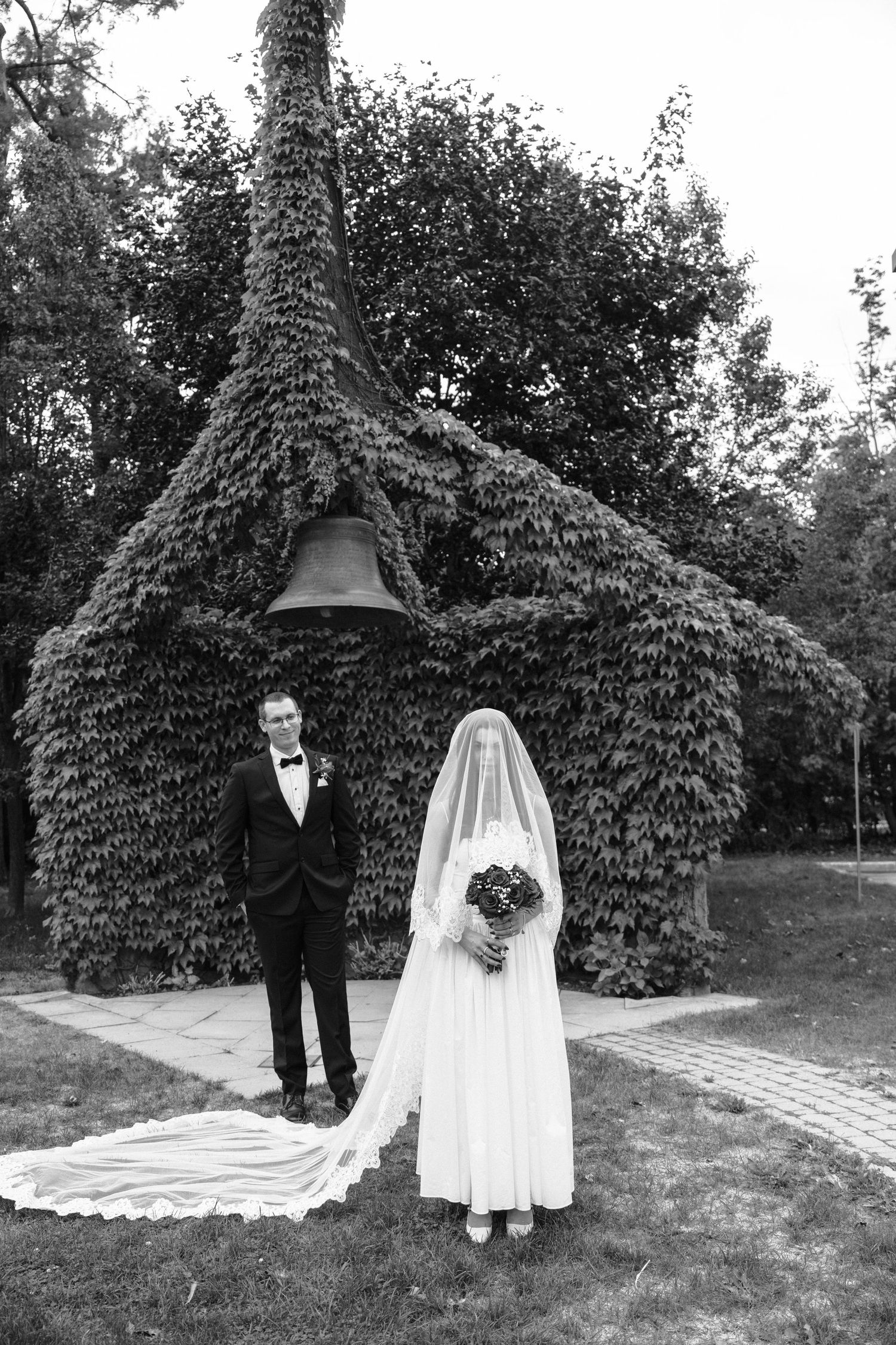 Wedding couple poses in three black and white photos under an ivy-covered archway in a garden setting.