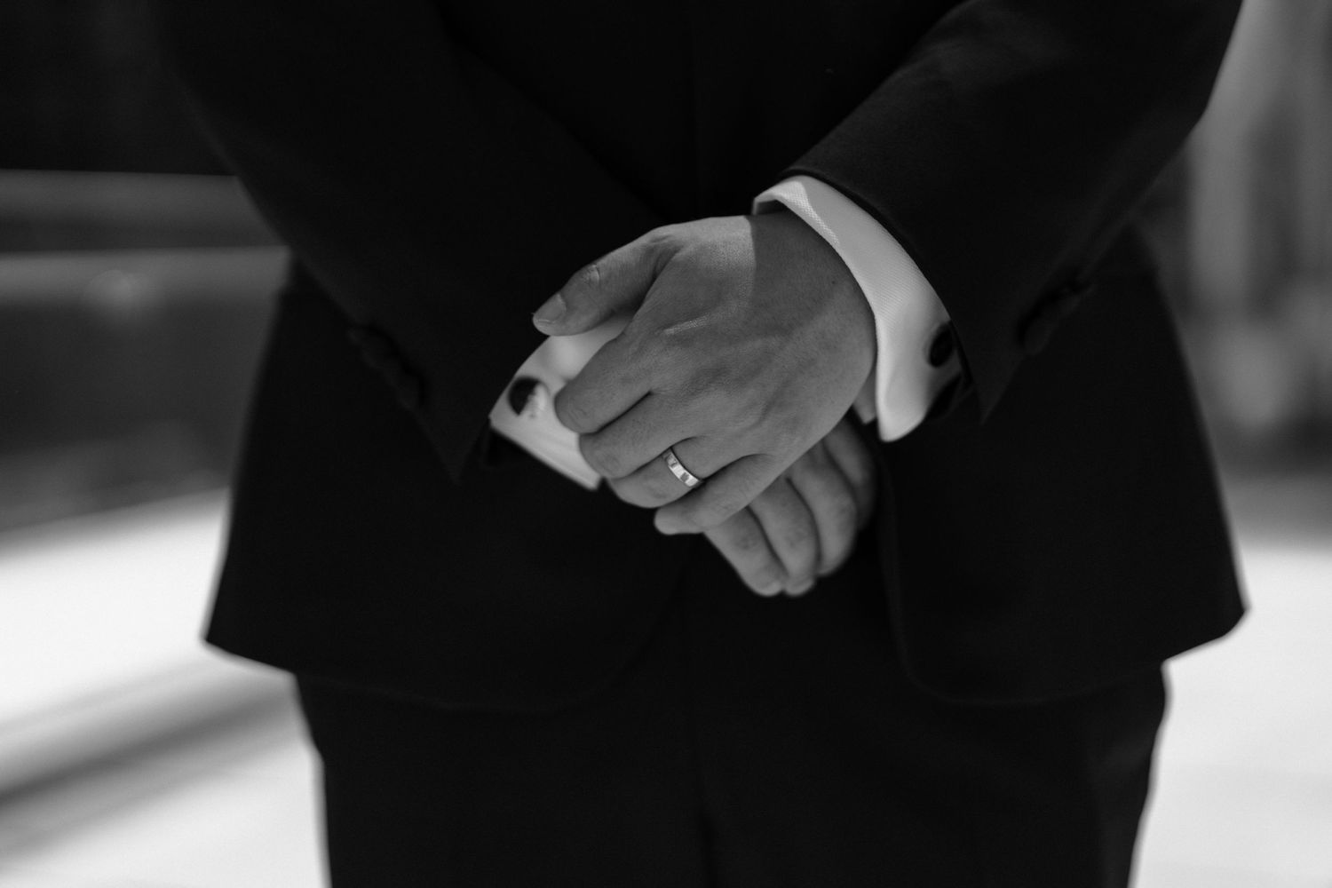 Close-up black and white photo of hands clasped together in formal wear showing professional business posture.