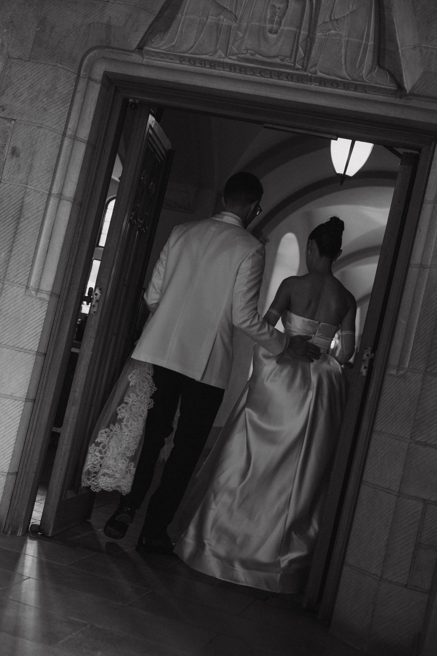A black and white photograph of a couple in formal attire entering through an elegant arched doorway.