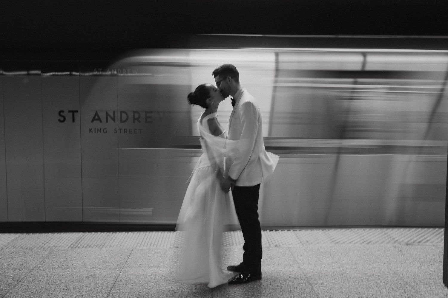 A romantic black and white couple embrace at a metro station with St Andre signage visible in background.