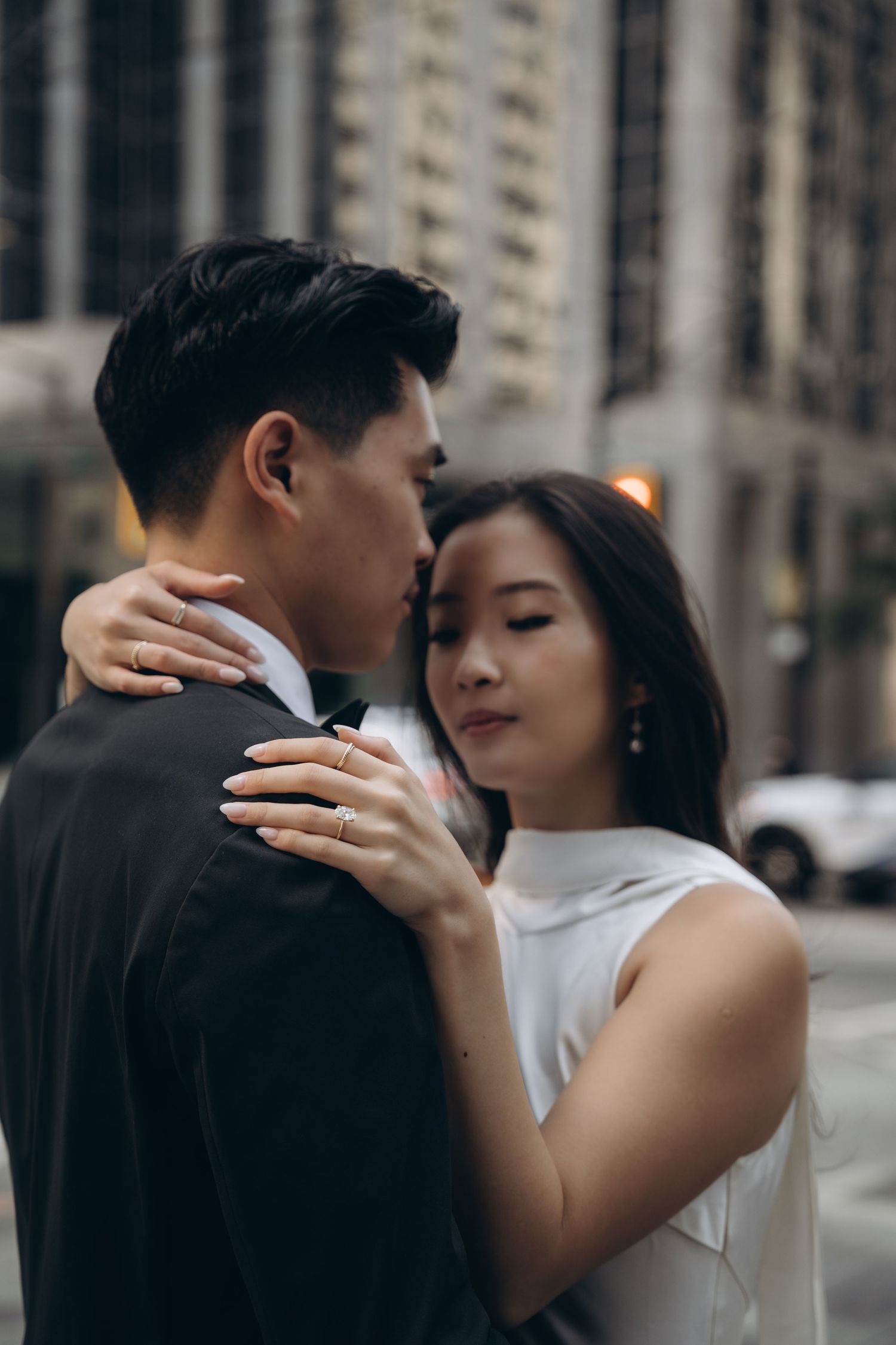 A romantic couple embraces in an intimate moment on a city street with tall buildings in the background.