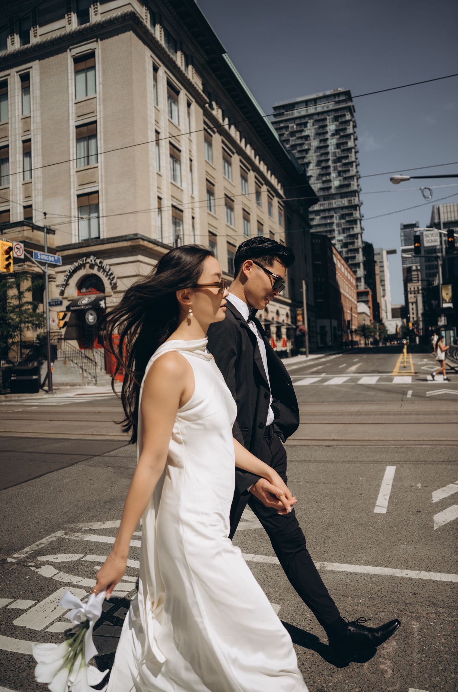 A couple in contrasting black and white outfits dance playfully on a city street intersection.