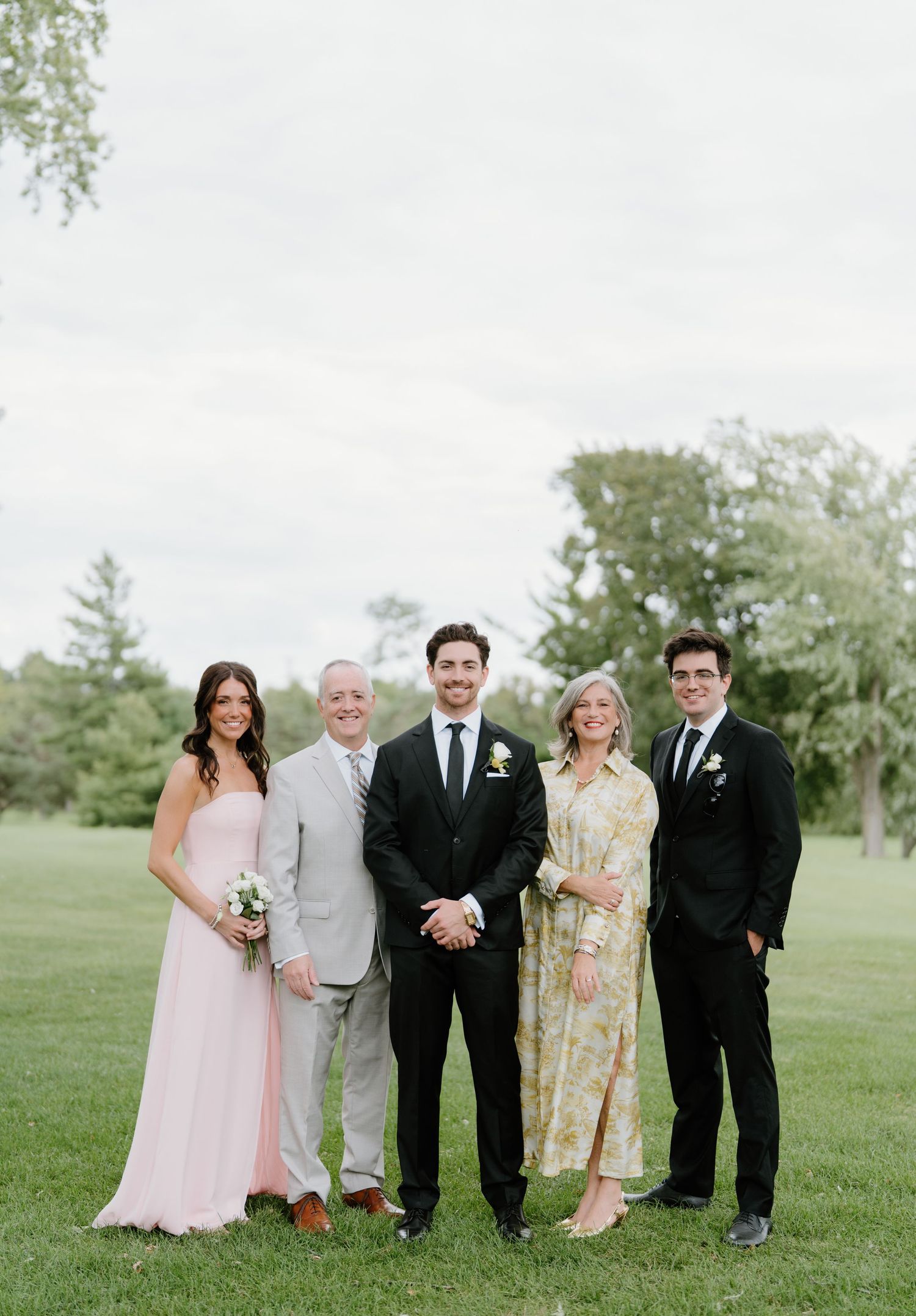 Wedding party members pose together on a lush green lawn during a spring outdoor celebration.