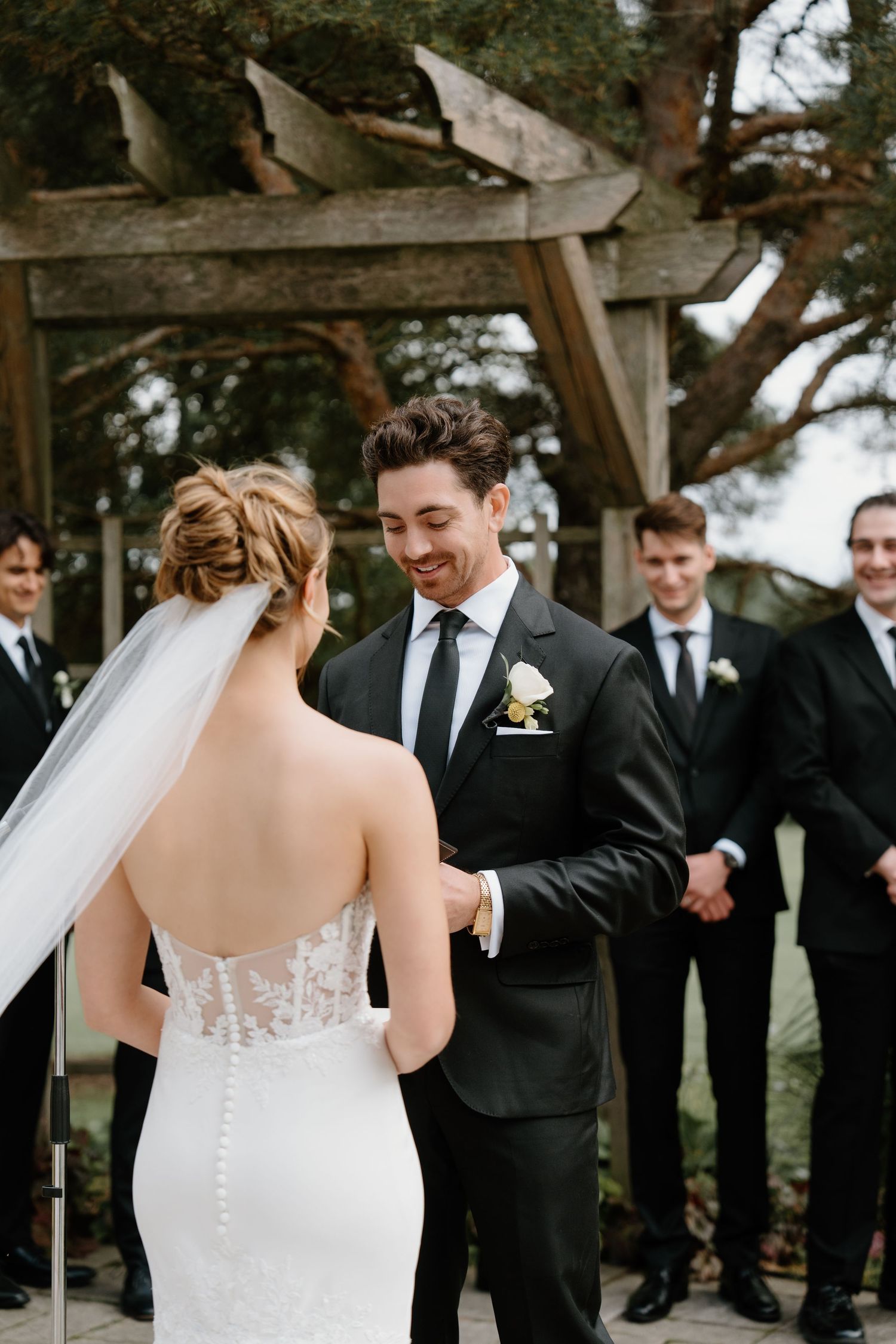 A bride and groom share their first look moment during an outdoor wedding ceremony with groomsmen in black suits.