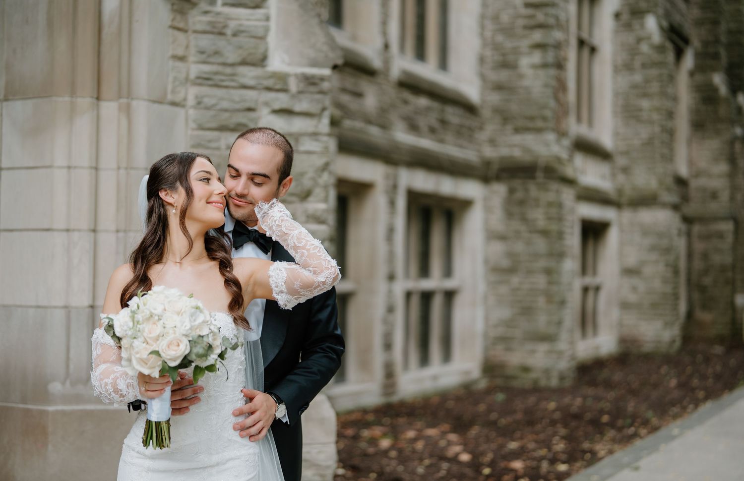 A romantic wedding moment captured as newlyweds embrace by a historic stone building.