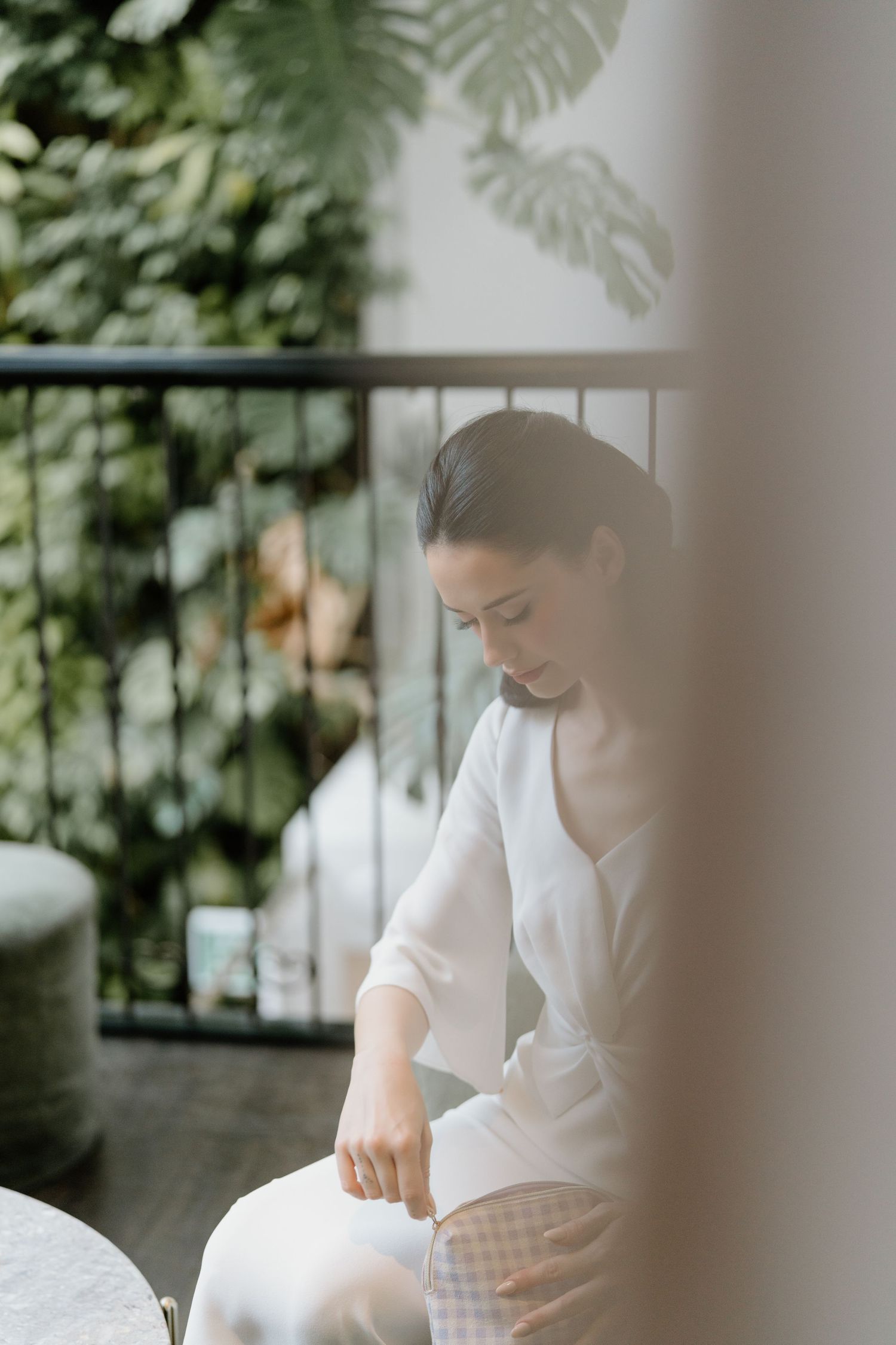 Person in white attire working at a table in a bright, plant-filled interior space.