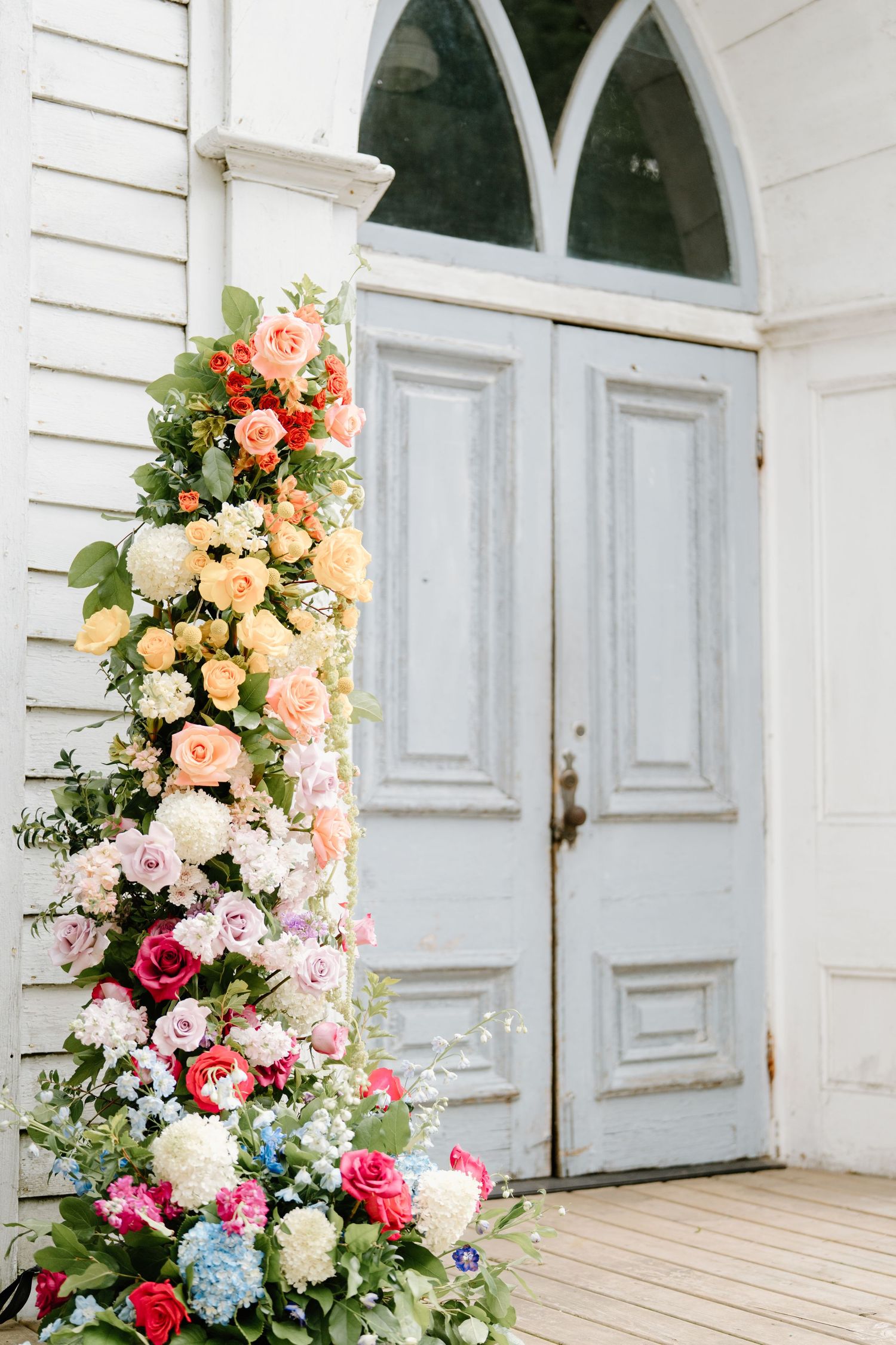 Elegant floral arrangements with pink, peach and white blooms decorate a white church entrance.