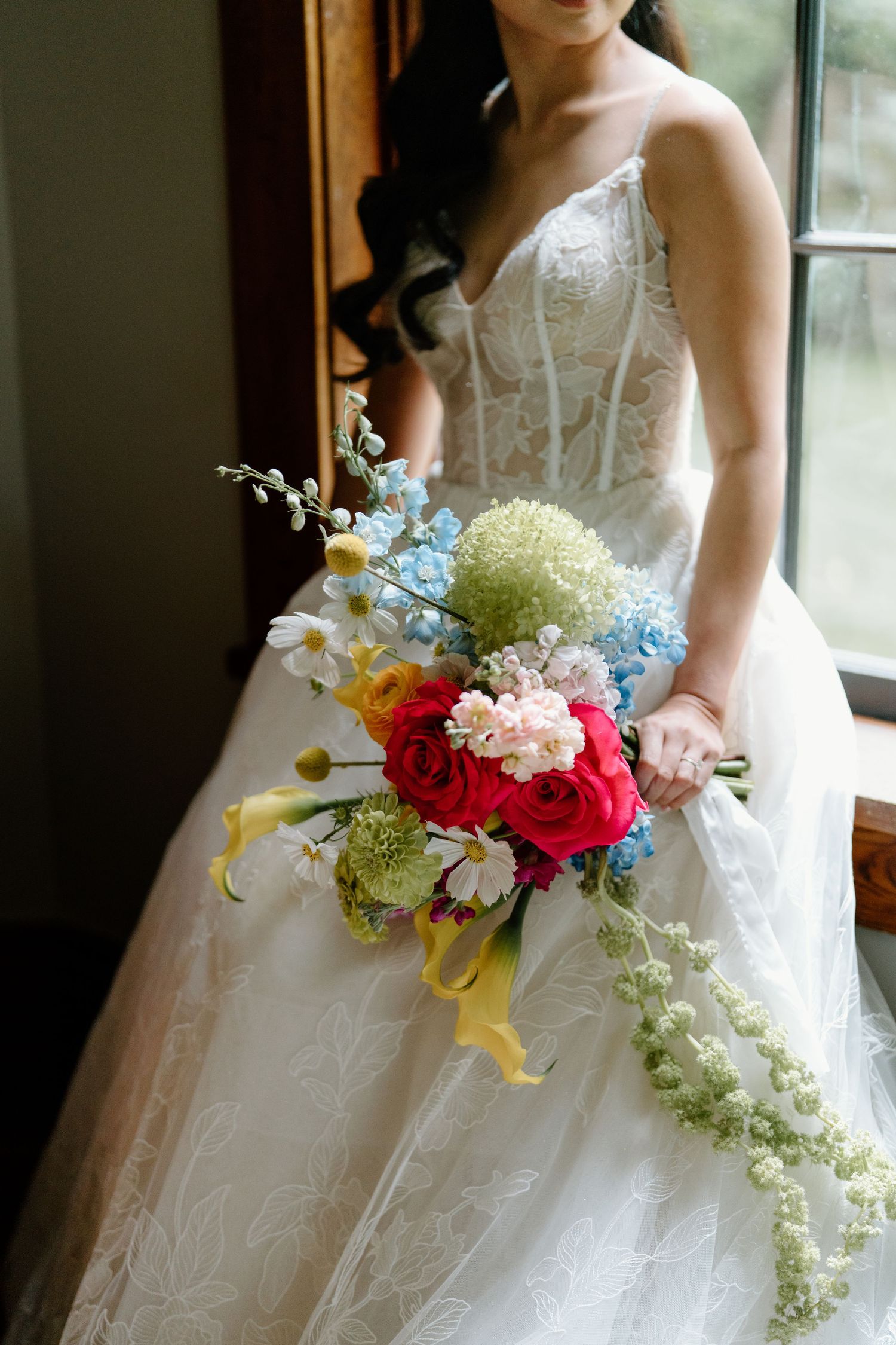 A cascading bridal bouquet features vibrant red and pink flowers with white orchids against a flowing white wedding gown.