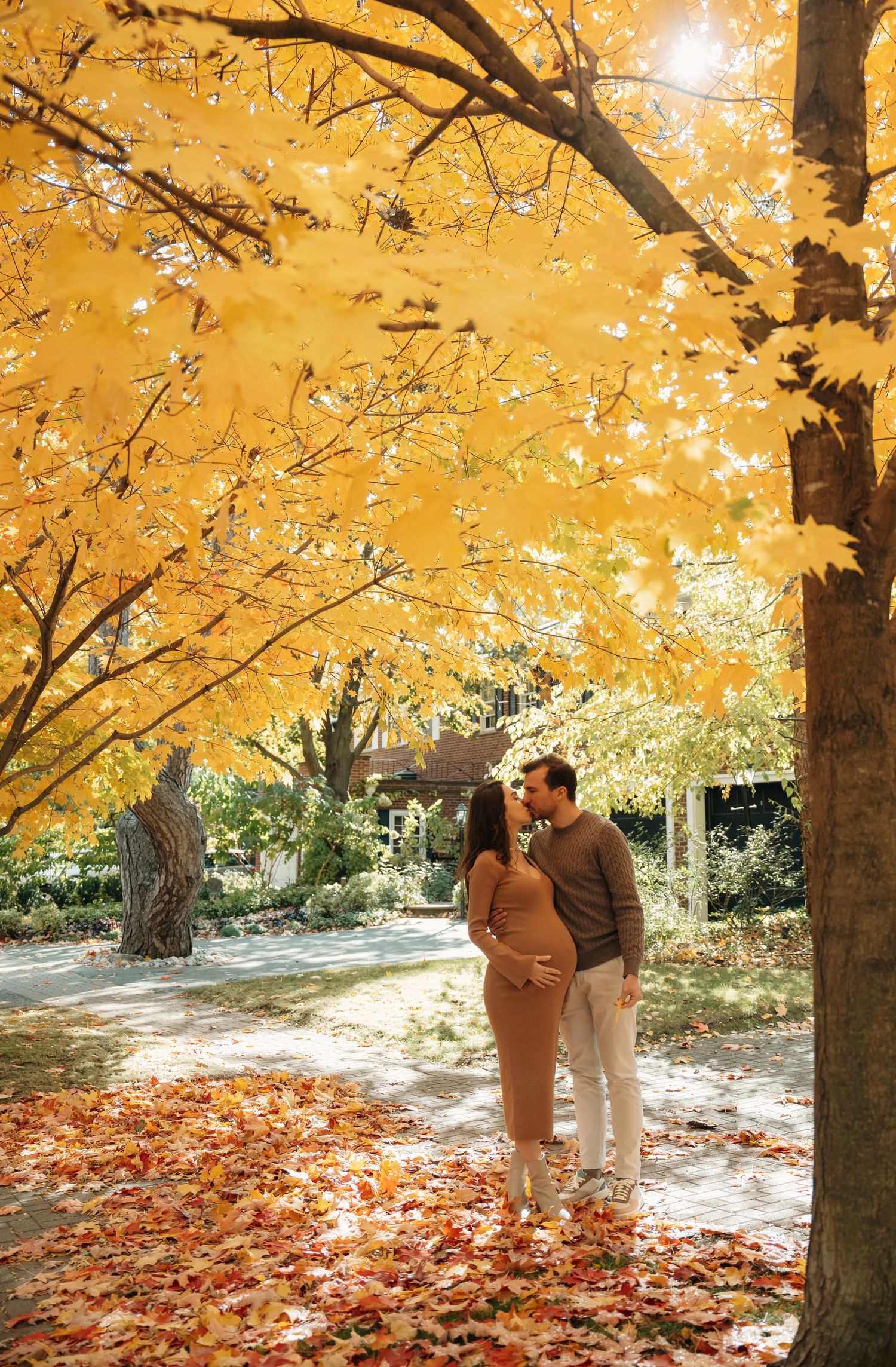 A couple embraces under beautiful golden fall foliage with autumn leaves scattered on the ground in a romantic setting.