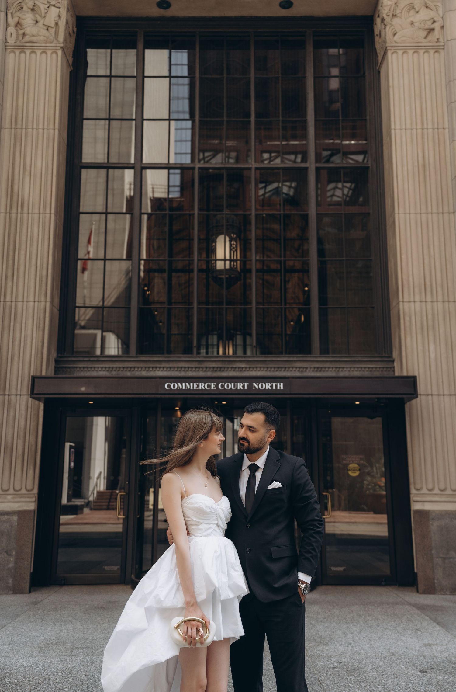 Romantic wedding couple in front of grand building pillars with groom in suit and bride in elegant white dress.