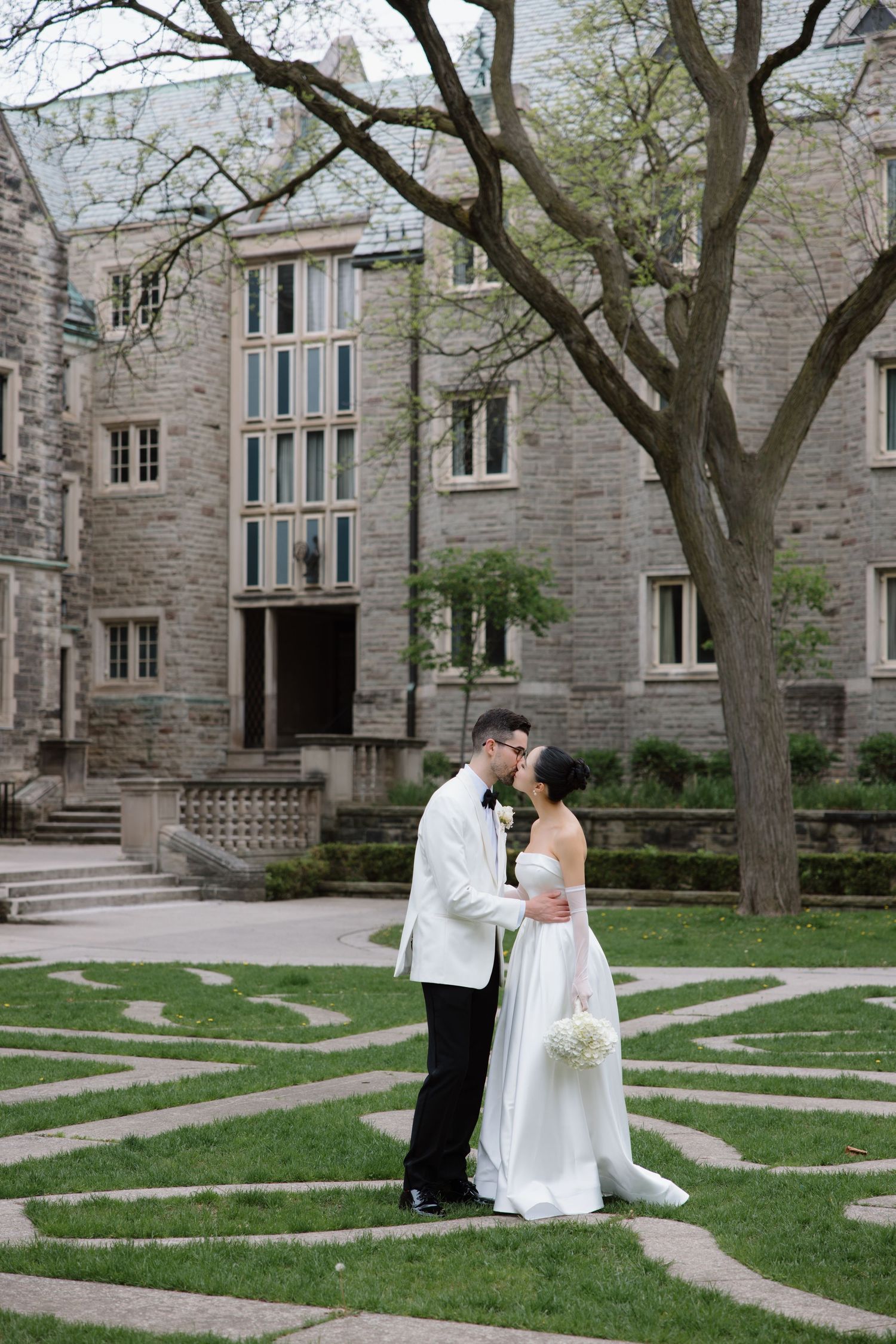 A wedding couple shares romantic moments in a series of photos taken outside a stone gothic building with manicured lawns.