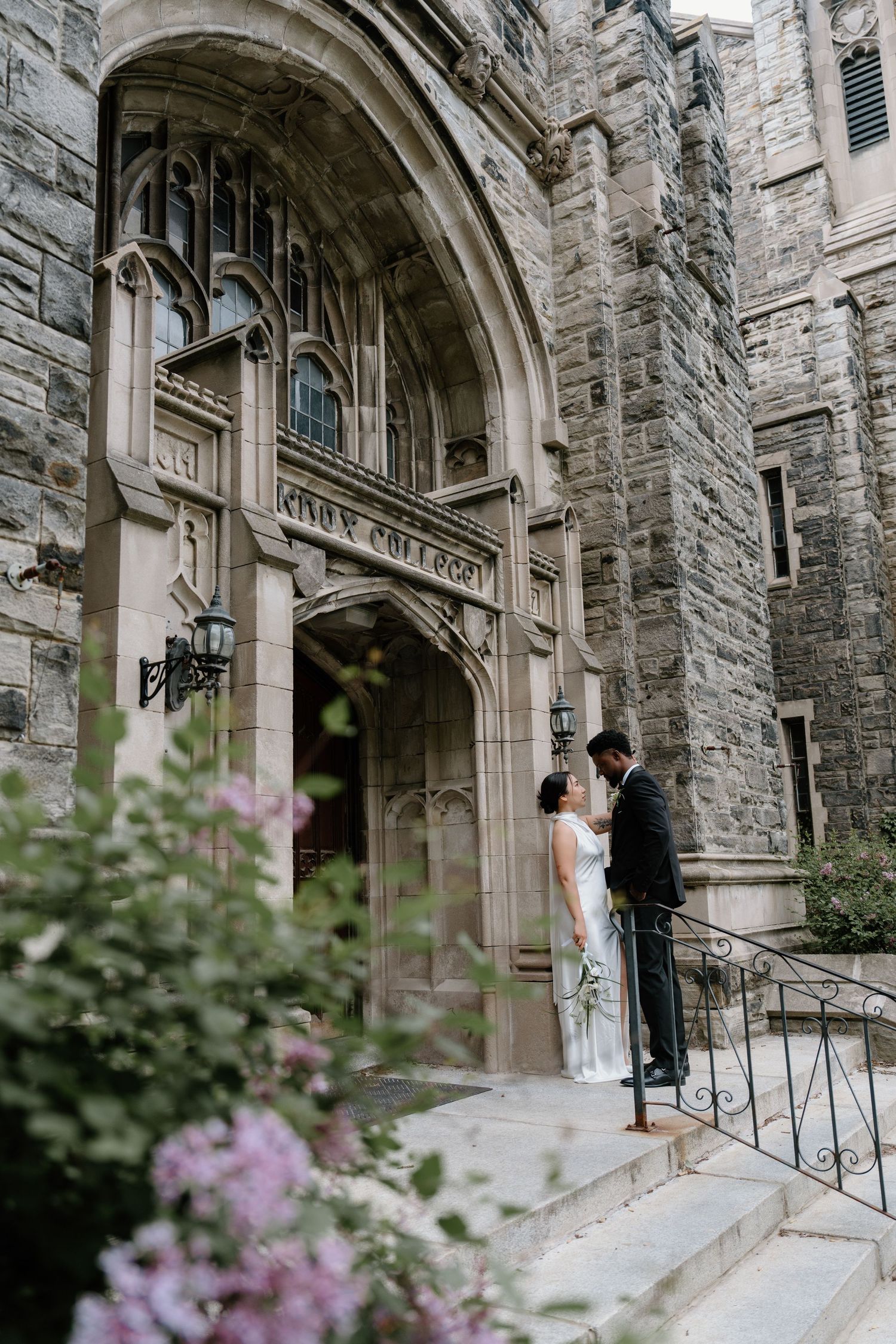 Elegant cathedral entrance with stone archway adorned with pink flowers blooming in the foreground.