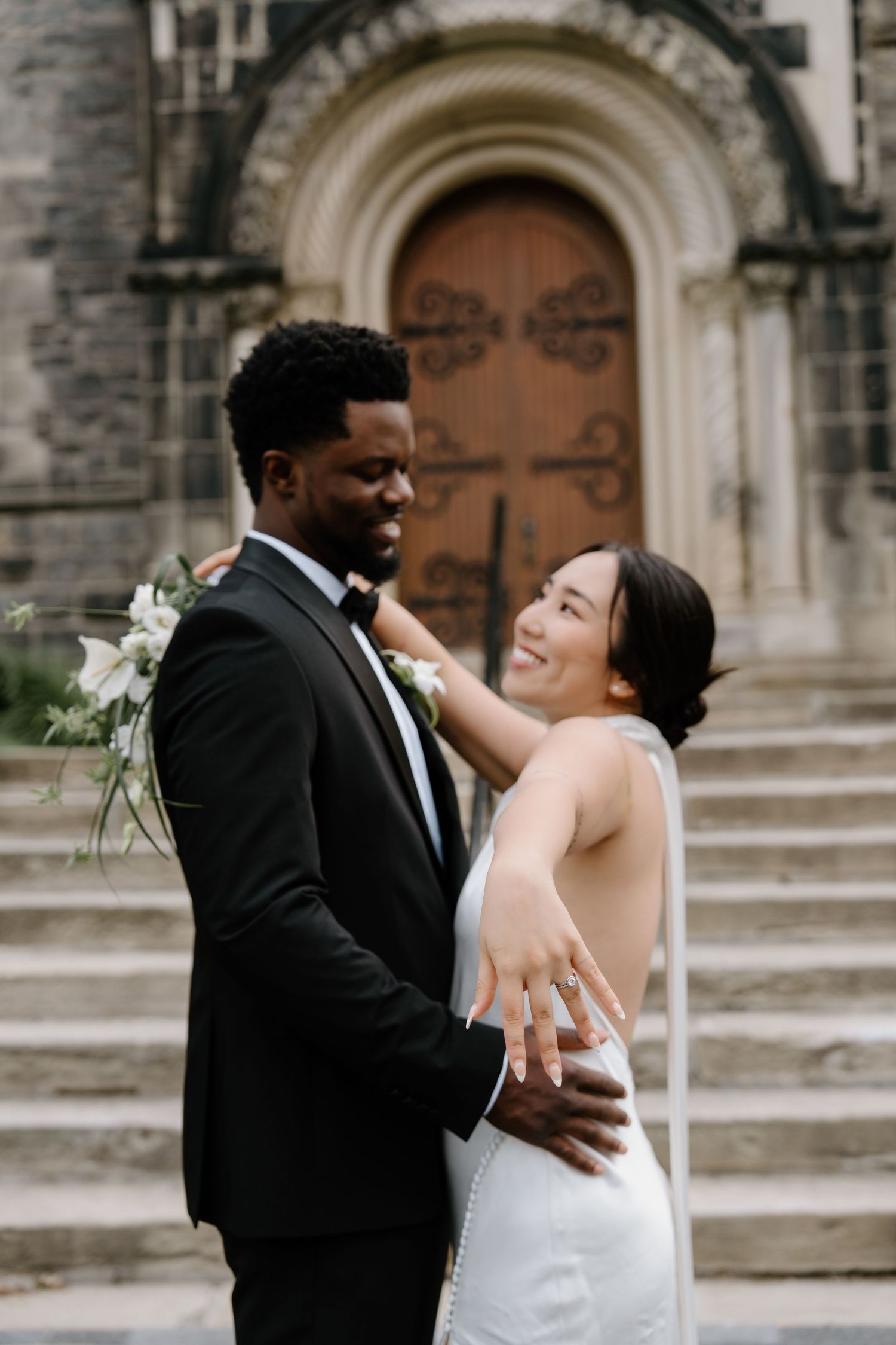 Newlyweds share an intimate moment and laughter outside a historic church with stone archways.