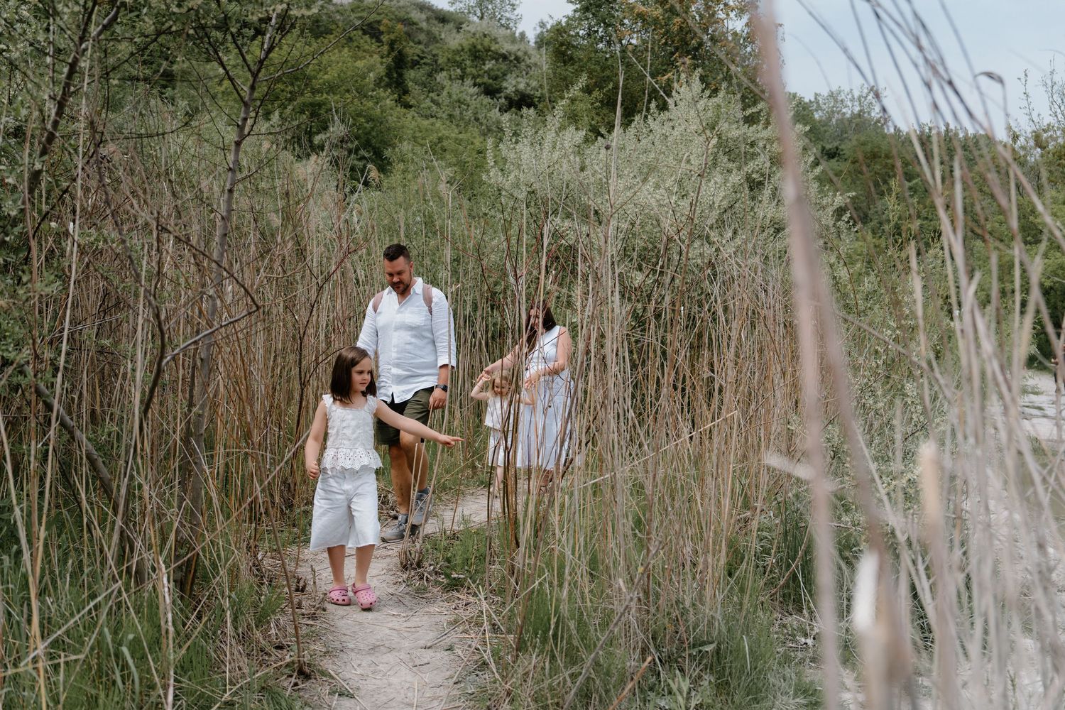 A couple walks down a scenic trail path through tall dried grasses and brush in a natural outdoor setting.
