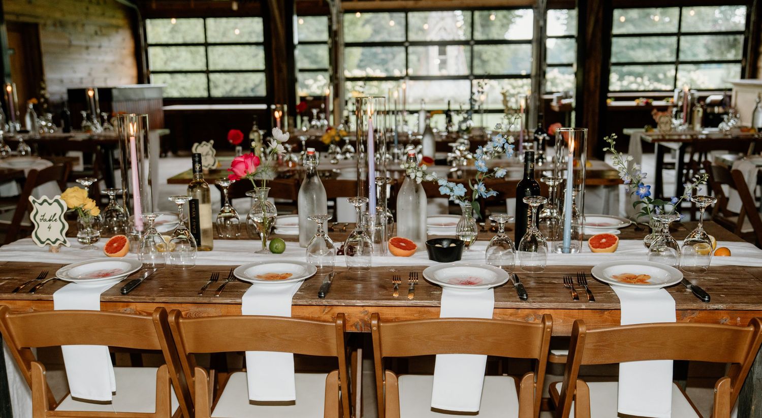 Long wooden dining tables set with glassware and place settings in an elegant restaurant interior.